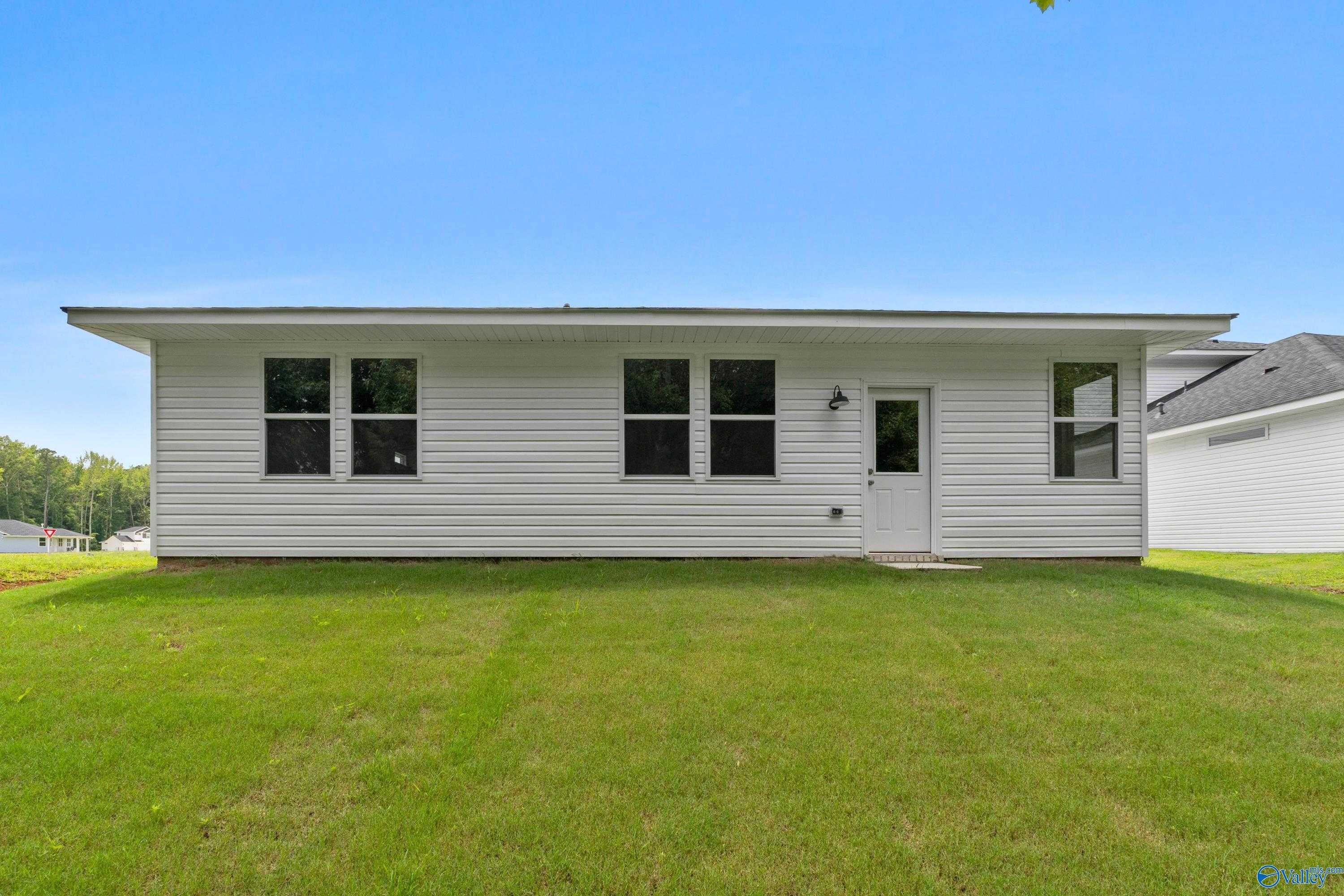 Rear view of The Phoenix 1-story home featuring white siding, double windows, entry door, and green backyard in Forest Glen, Hazel Green, Alabama