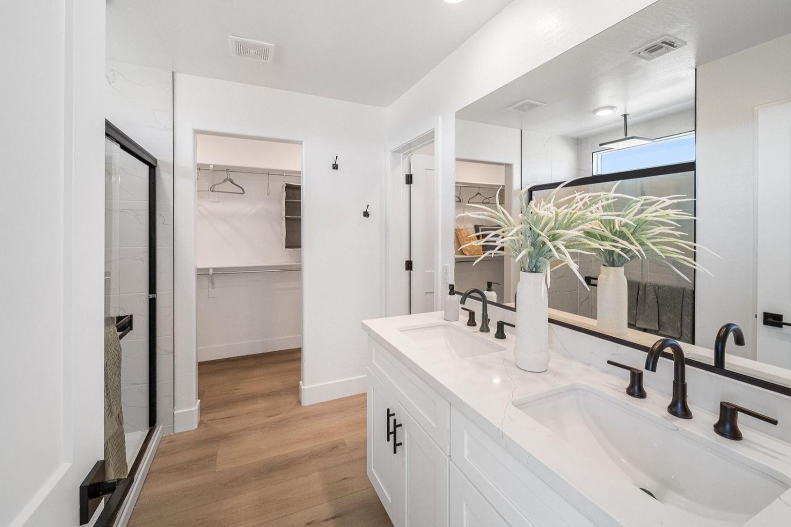 Spacious master bathroom at South Ranch Southern Collection in Prescott AZ with white double vanity, black-framed walk-in shower, and adjacent closet