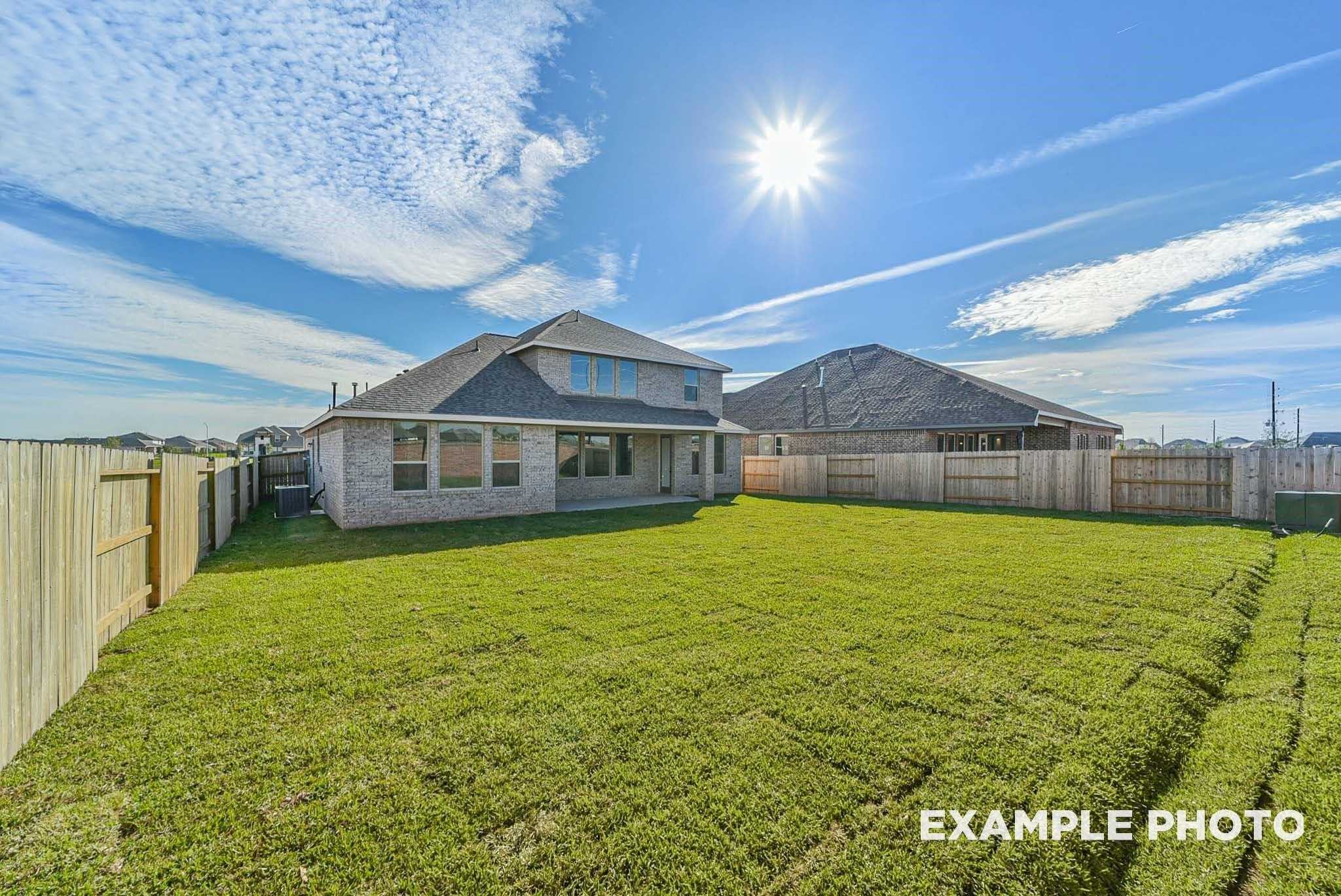 Spacious backyard with lush green lawn, covered patio, and brick single-story home in Davidson Homes The Philip C, Rosharon, Texas