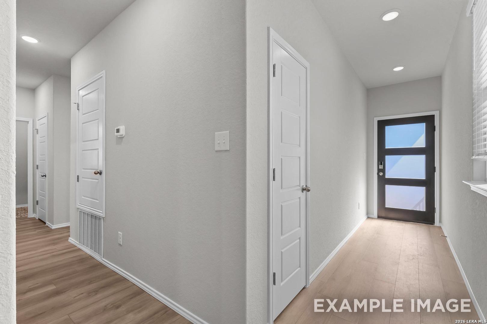 Bright entry hallway with white doors, gray walls, recessed lights, and hardwood floors in Davidson Homes The Colorado D, San Antonio