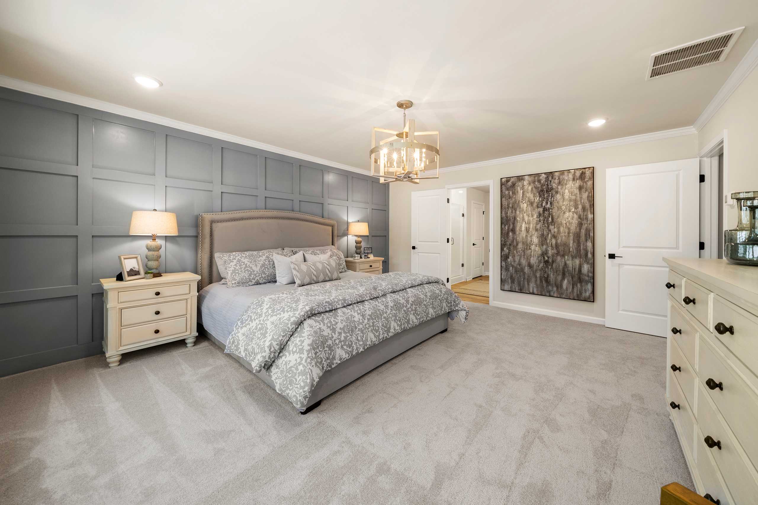 Spacious primary bedroom at Reverie at East Lake in McDonough GA with gray shiplap accent wall, king bed, chandelier, and abstract art