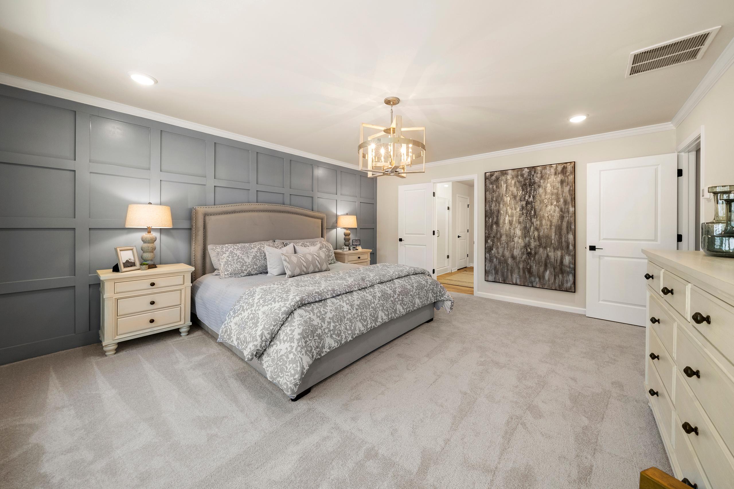 Spacious primary bedroom at Reverie at East Lake in McDonough GA with gray shiplap accent wall, king bed, chandelier, and abstract art
