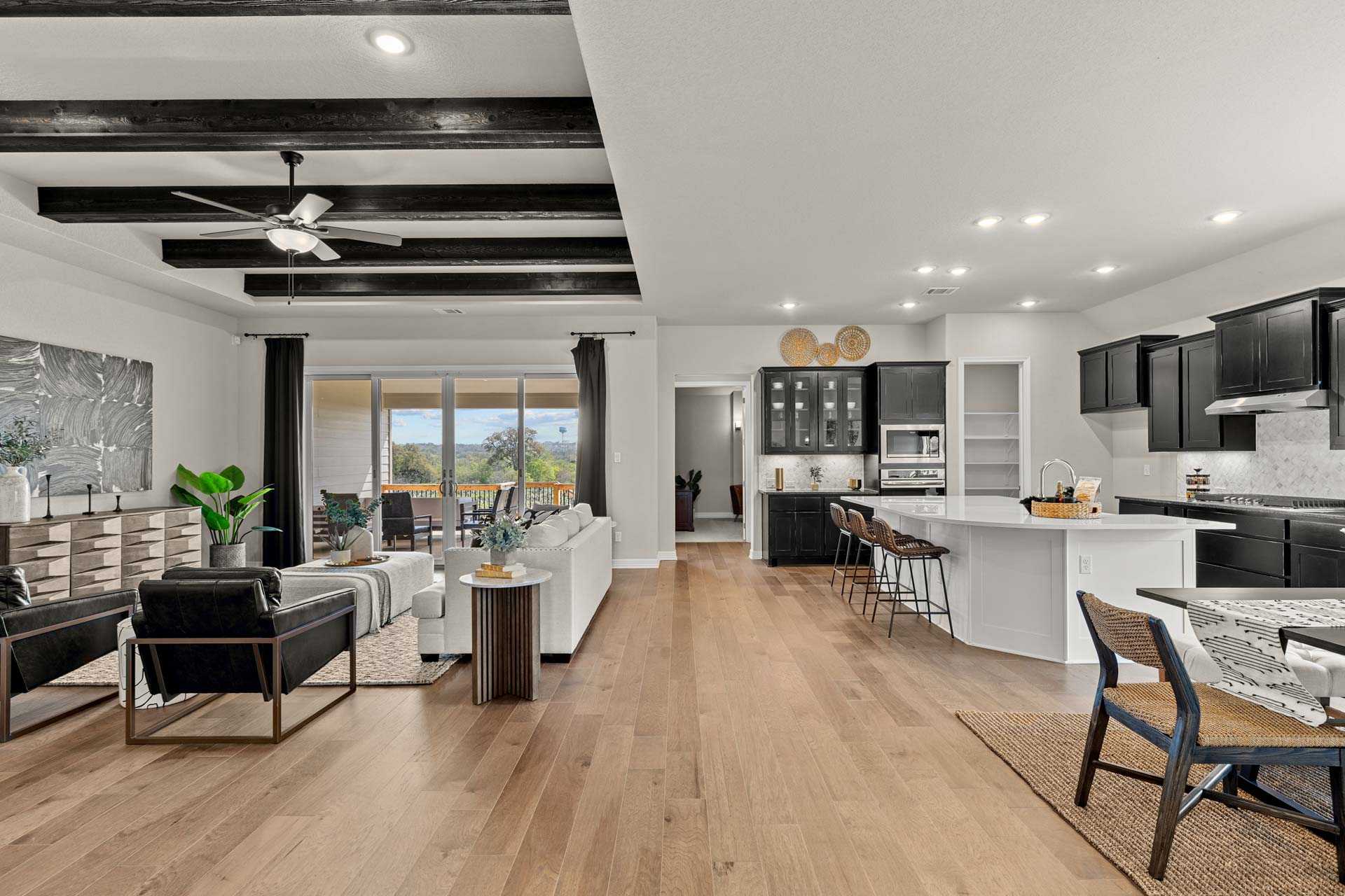 Open-concept living and kitchen in The Summerlin B with black beamed ceiling, white island, and patio views