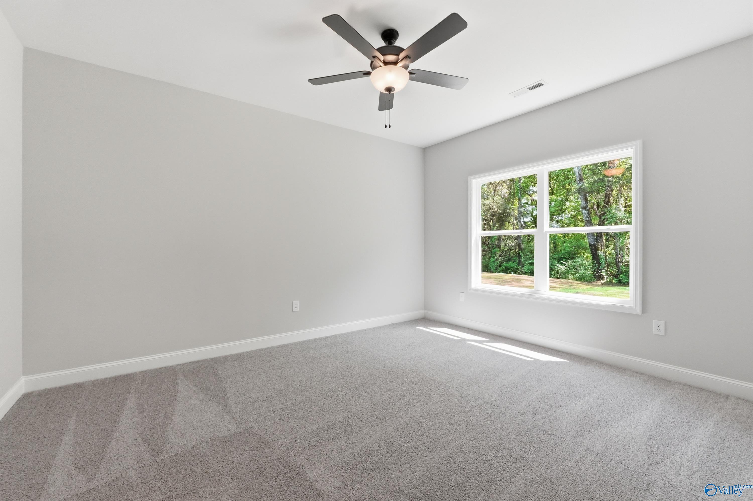 Bright bedroom with gray walls, carpet floor, lighted ceiling fan, and large window to lush green trees in The Franklin, Huntsville home