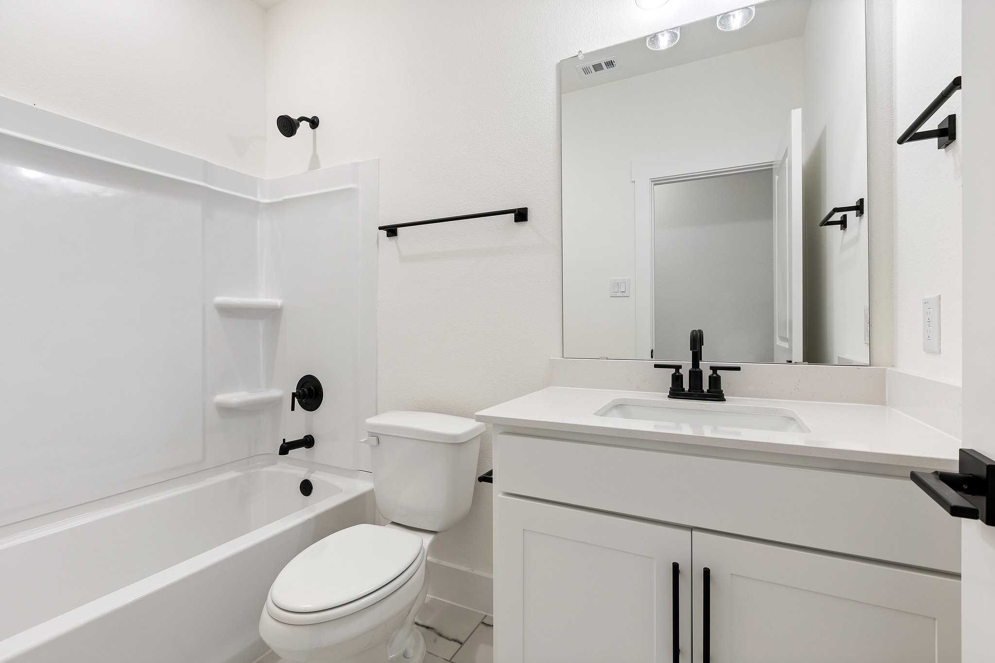 Modern white guest bathroom with tub-shower combo, vanity, and black fixtures in Davidson Homes Rockford C, Josephine, TX