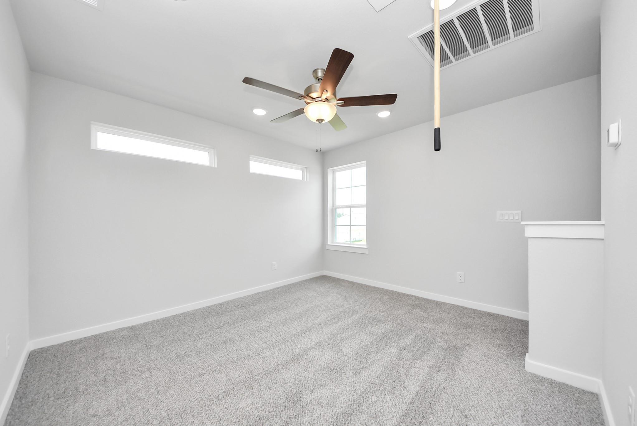 Bright, spacious bedroom with ceiling fan and transom windows in The Sabine E floor plan at Windmill Estates, Magnolia.