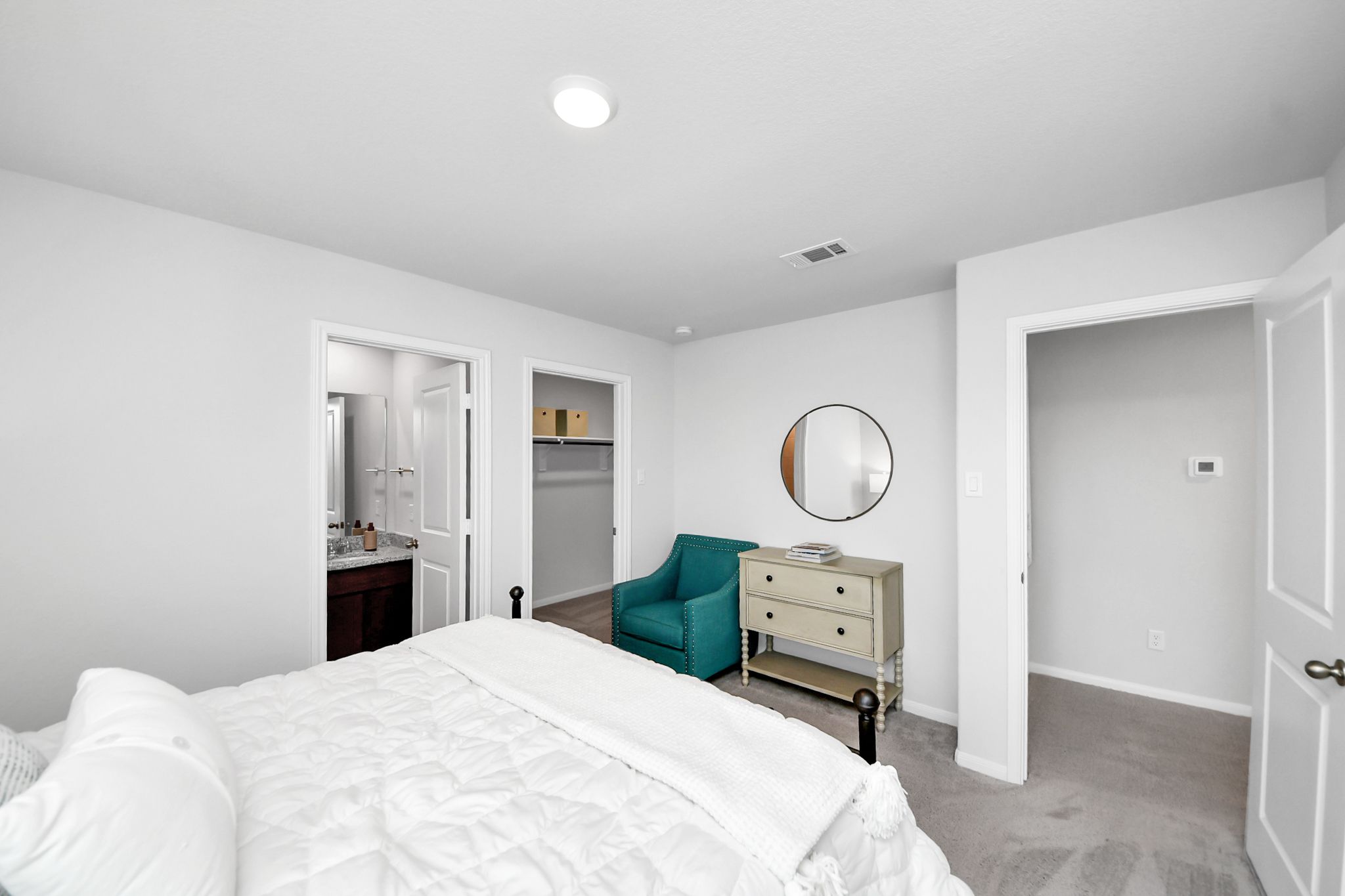 Spacious bedroom at Sunterra in Katy, TX by Davidson Homes featuring a white bed, teal accent chair, and en-suite bathroom.