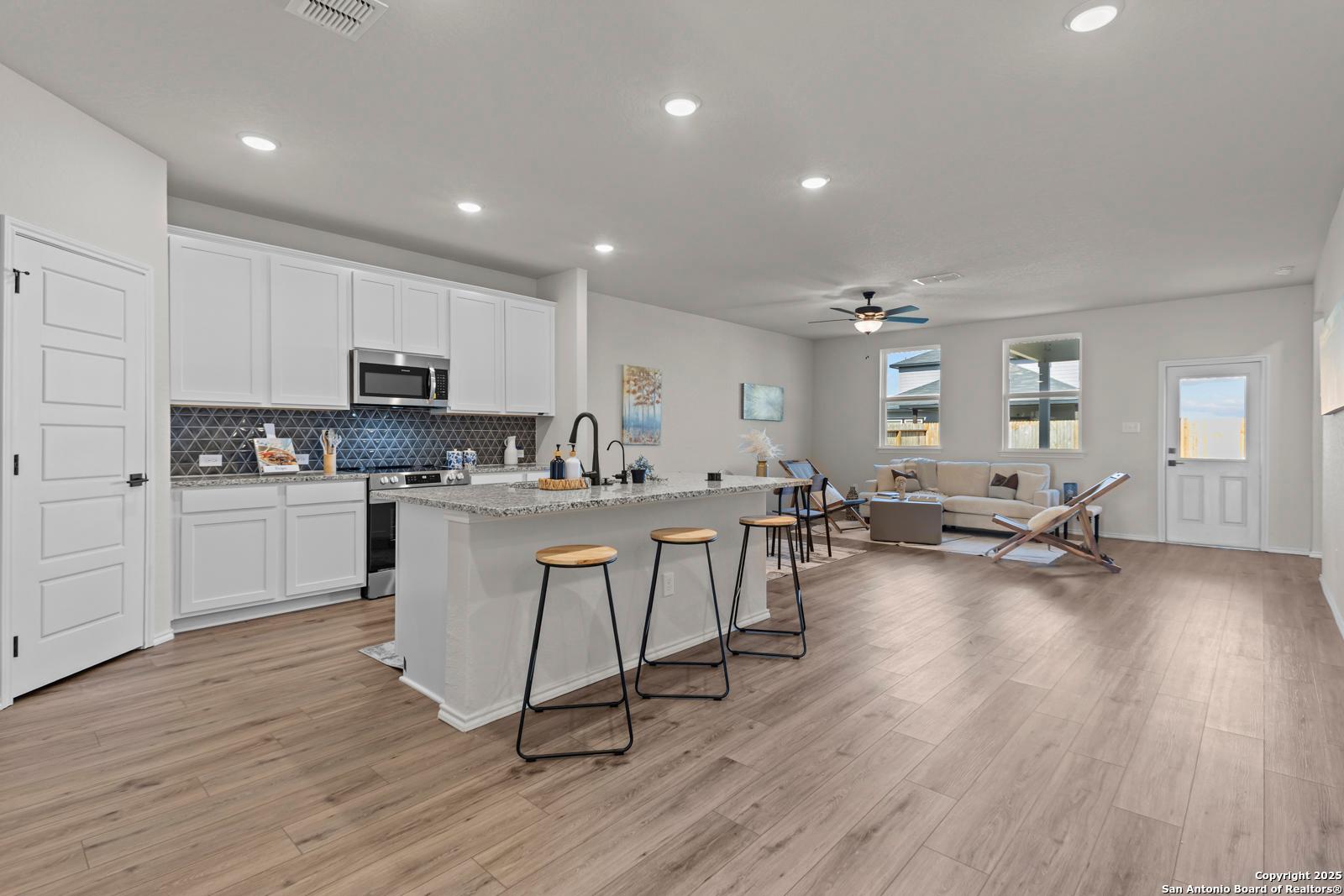Open-concept kitchen with white cabinets, black subway backsplash, island bar, and adjacent living space in Davidson Homes The Douglas C, Seguin, Texas