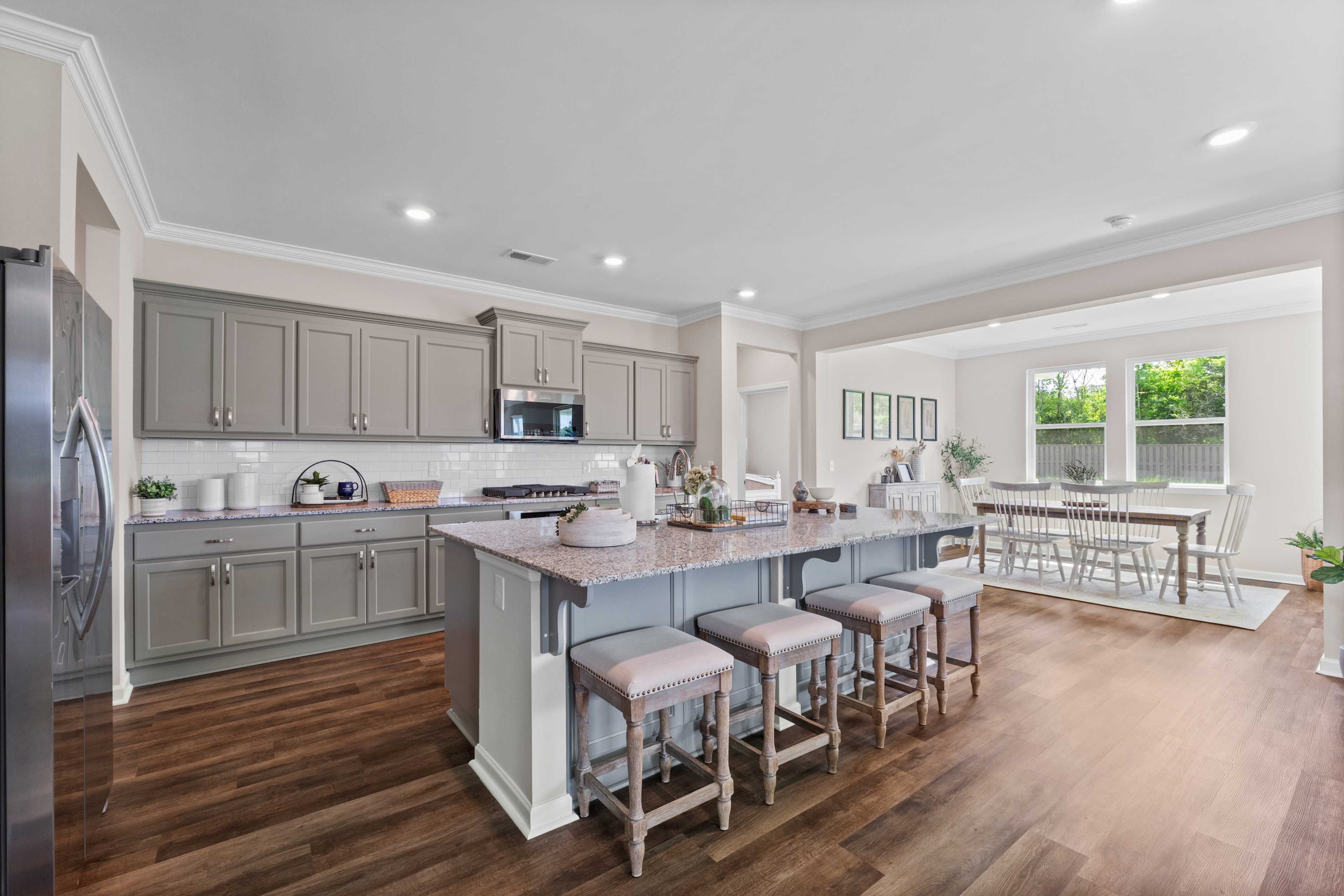 Spacious gray kitchen at Riverton Preserve in Huntsville AL with large center island, bar stools, stainless appliances, and open dining area