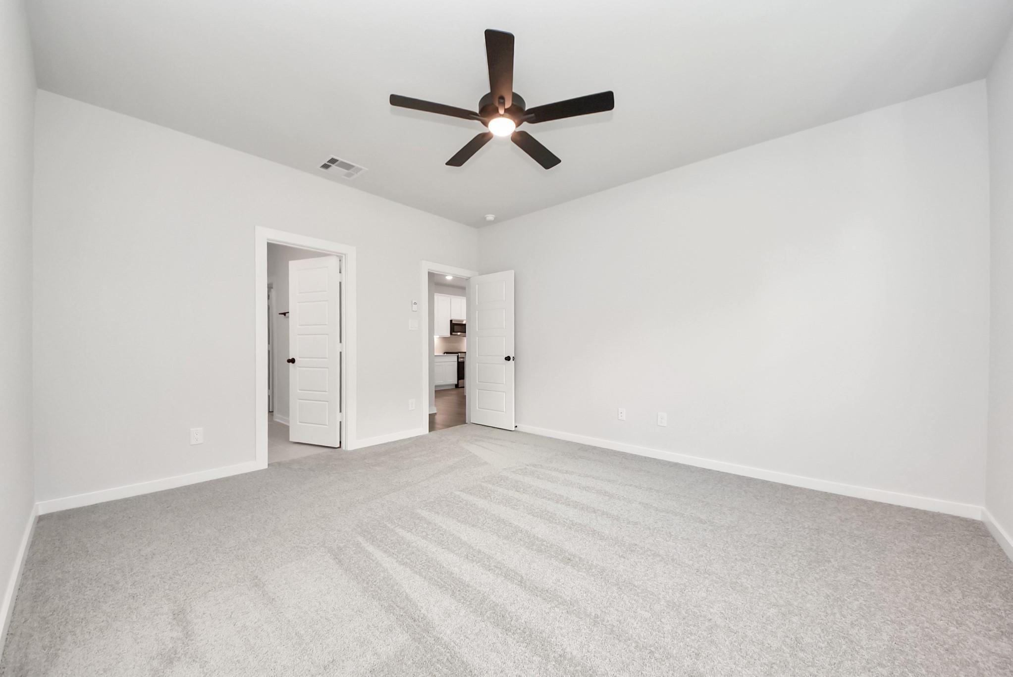 Spacious bedroom with grey carpet and ceiling fan in The Daphne F floor plan at Sundance Cove in Crosby, Texas.