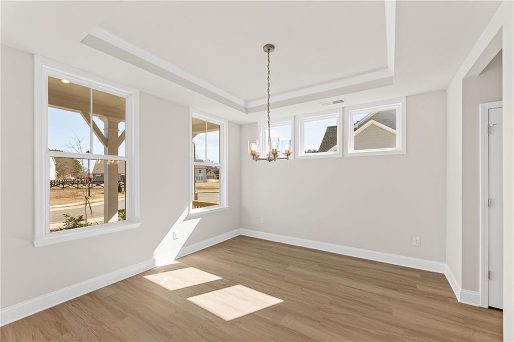Bright sunlit room with tray ceiling, chandelier, hardwood floors, and large windows in Davidson Homes Willow B, Hoschton, GA