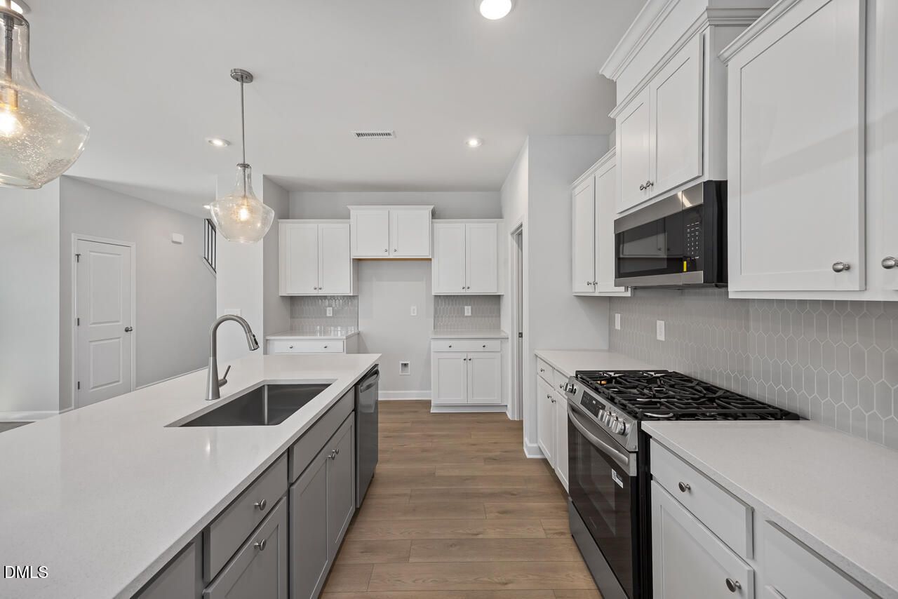 Modern kitchen with white cabinets, quartz countertops, and stainless appliances in The Adalynn B, Gregory Village, Lillington.