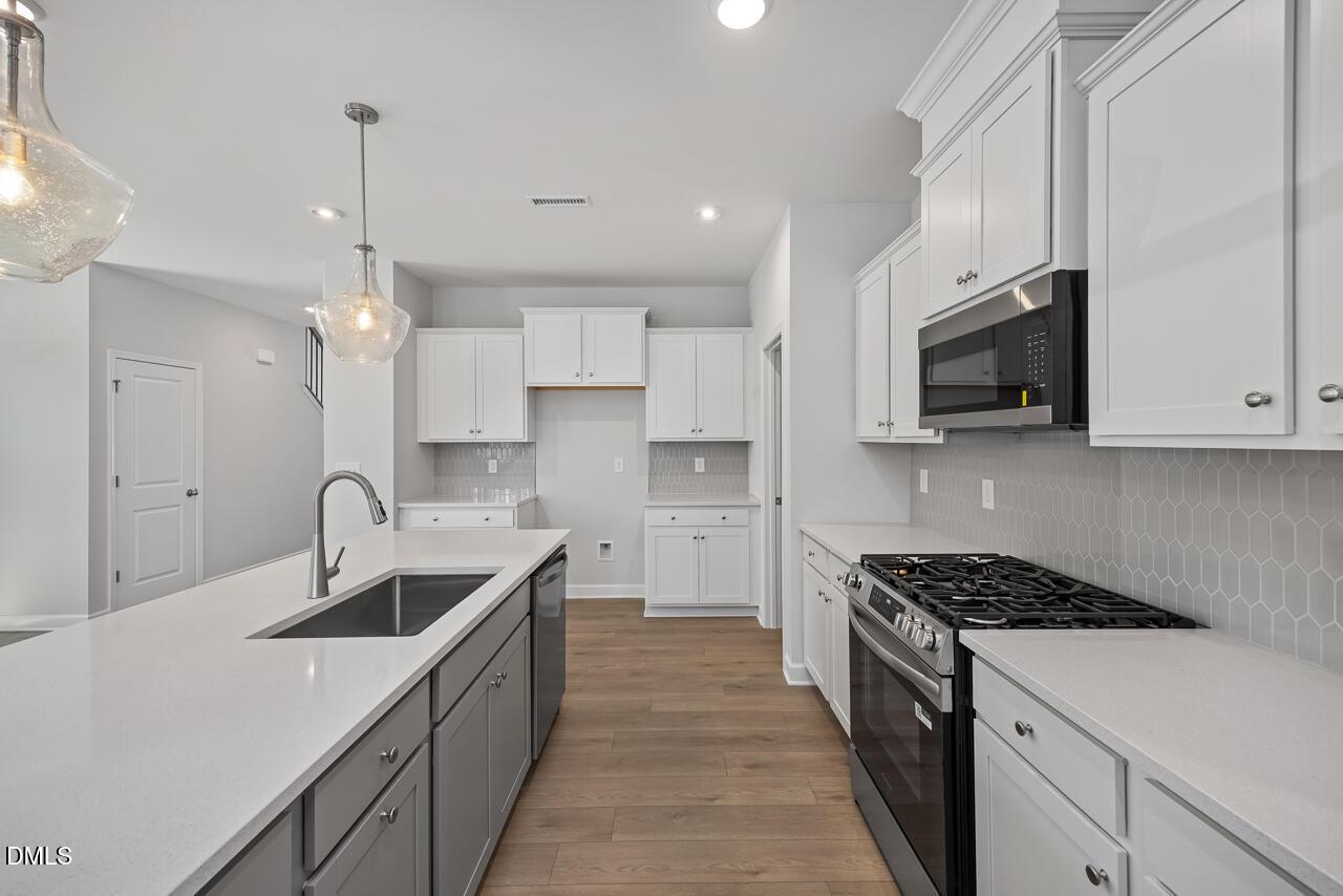 Modern kitchen with white cabinets, quartz countertops, and stainless appliances in The Adalynn B, Gregory Village, Lillington.