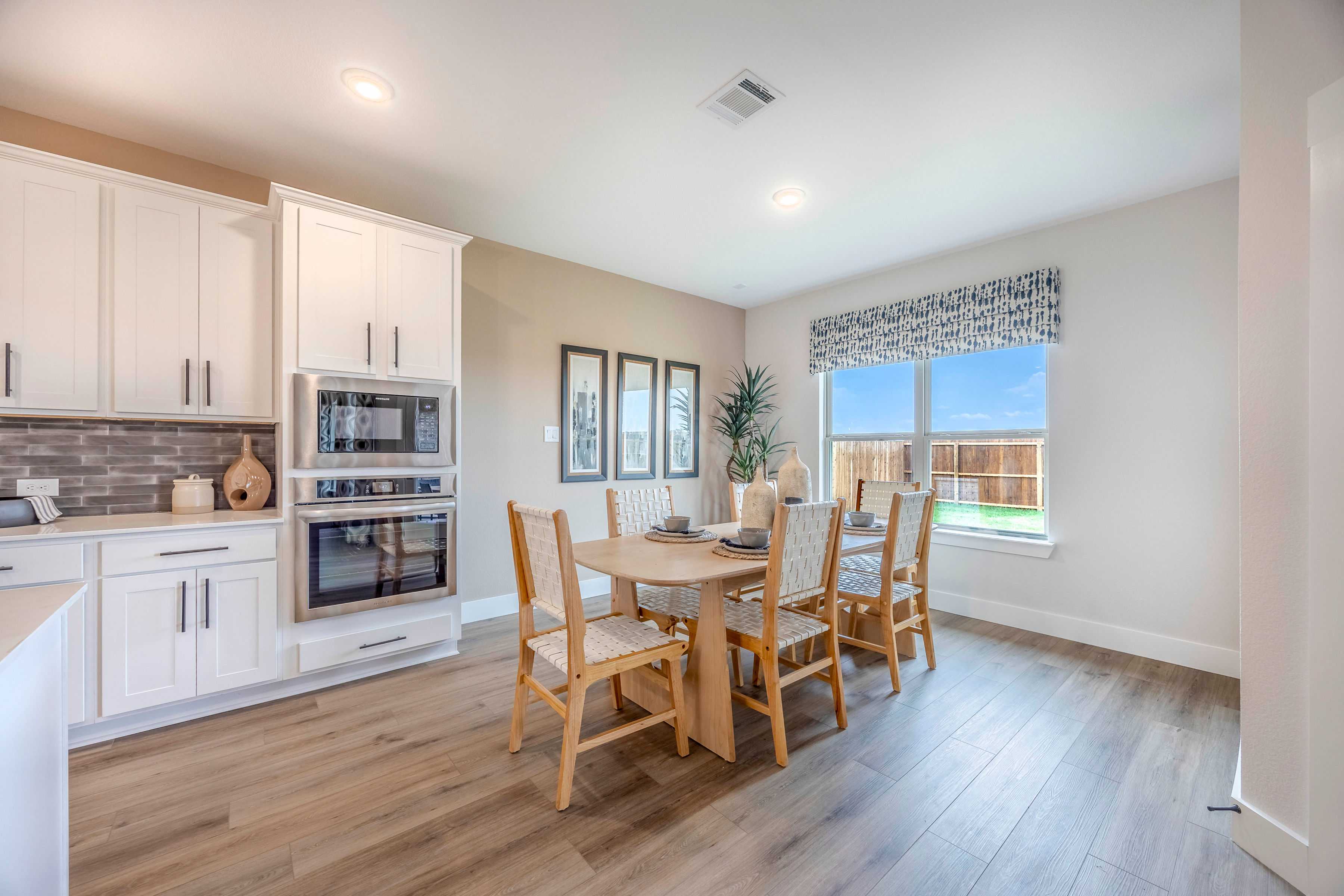 Spacious dining room in The Rockford with oak table, white shaker cabinets, double ovens, and window to backyard