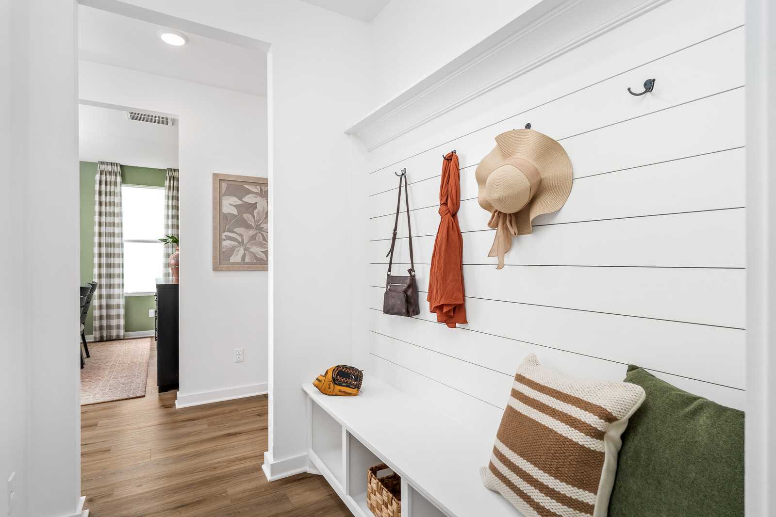 Spacious mudroom with white shiplap walls, hook storage for hats and bags, cushioned bench at Calista Farms in White House Tennessee