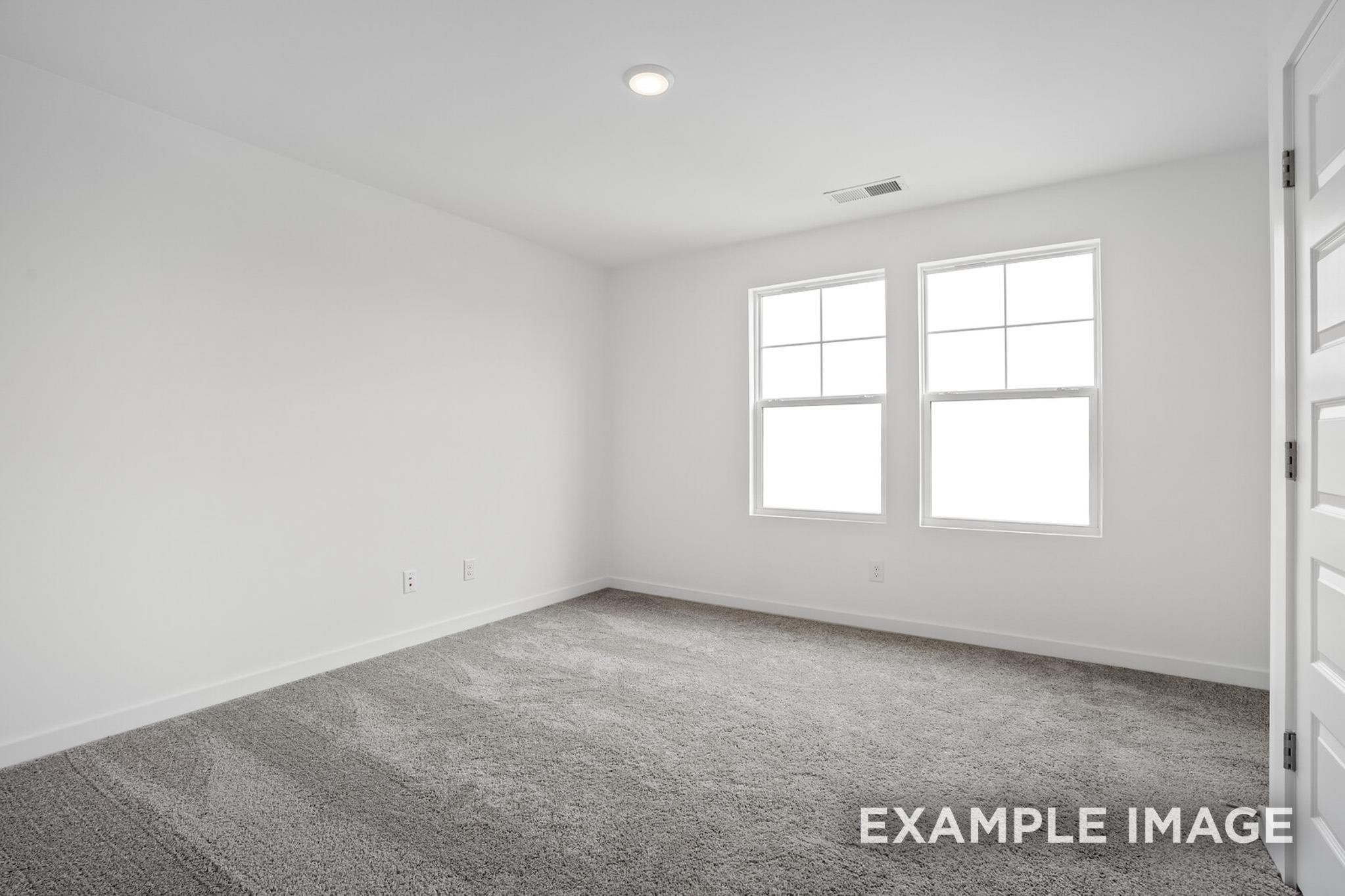 Spacious empty bedroom in The Logan C featuring white walls, gray carpet, double windows, and closet doors