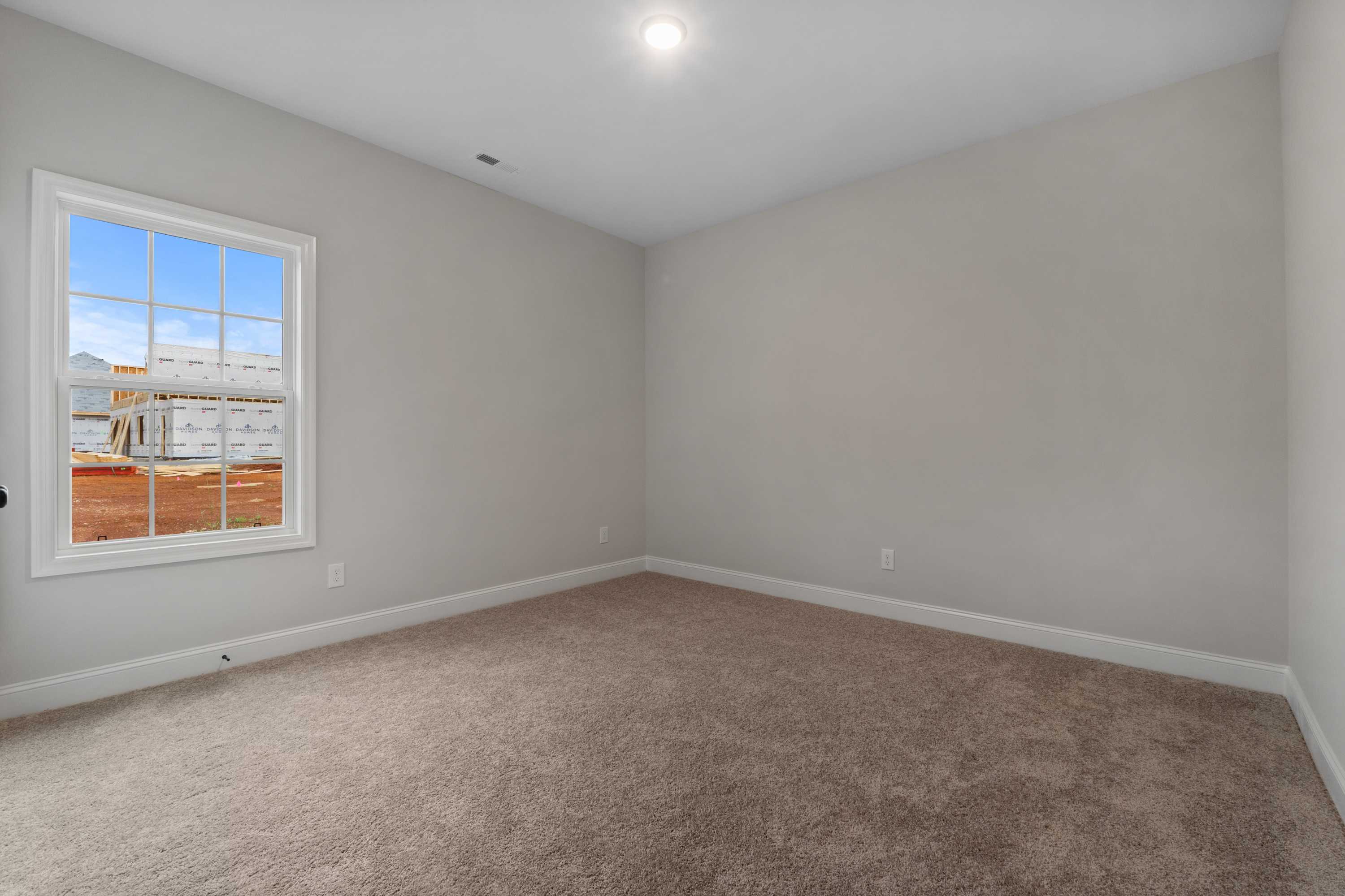 Spacious secondary bedroom in The Oxford home design with neutral gray walls, large window, and plush beige carpet