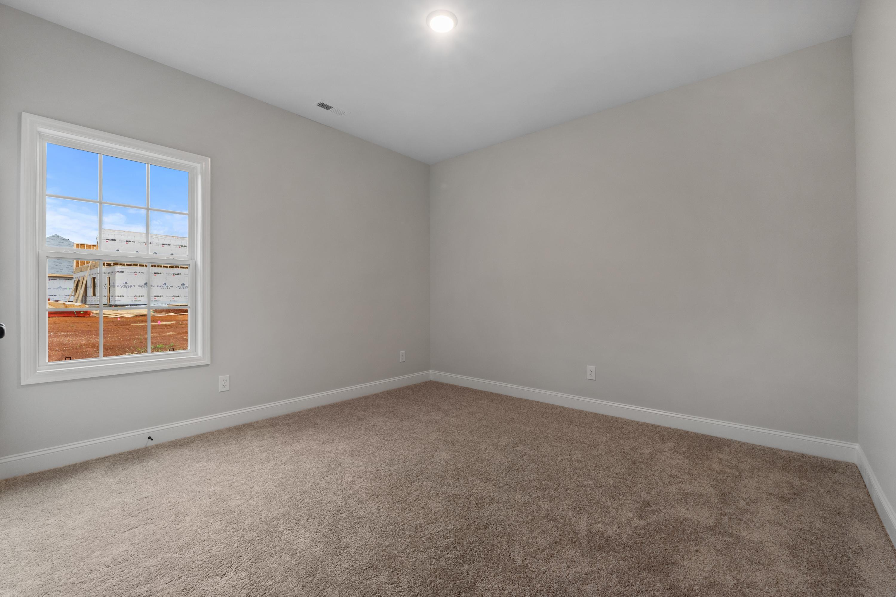 Spacious secondary bedroom in The Oxford home design with neutral gray walls, large window, and plush beige carpet