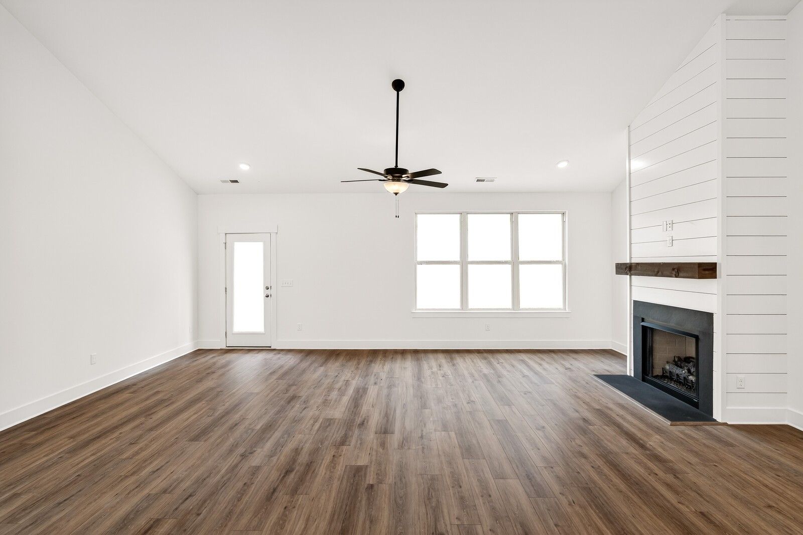 Bright living room with shiplap fireplace wall, large triple windows, ceiling fan, and hardwood floors in Davidson Homes Ridgeport C, Gallatin, TN