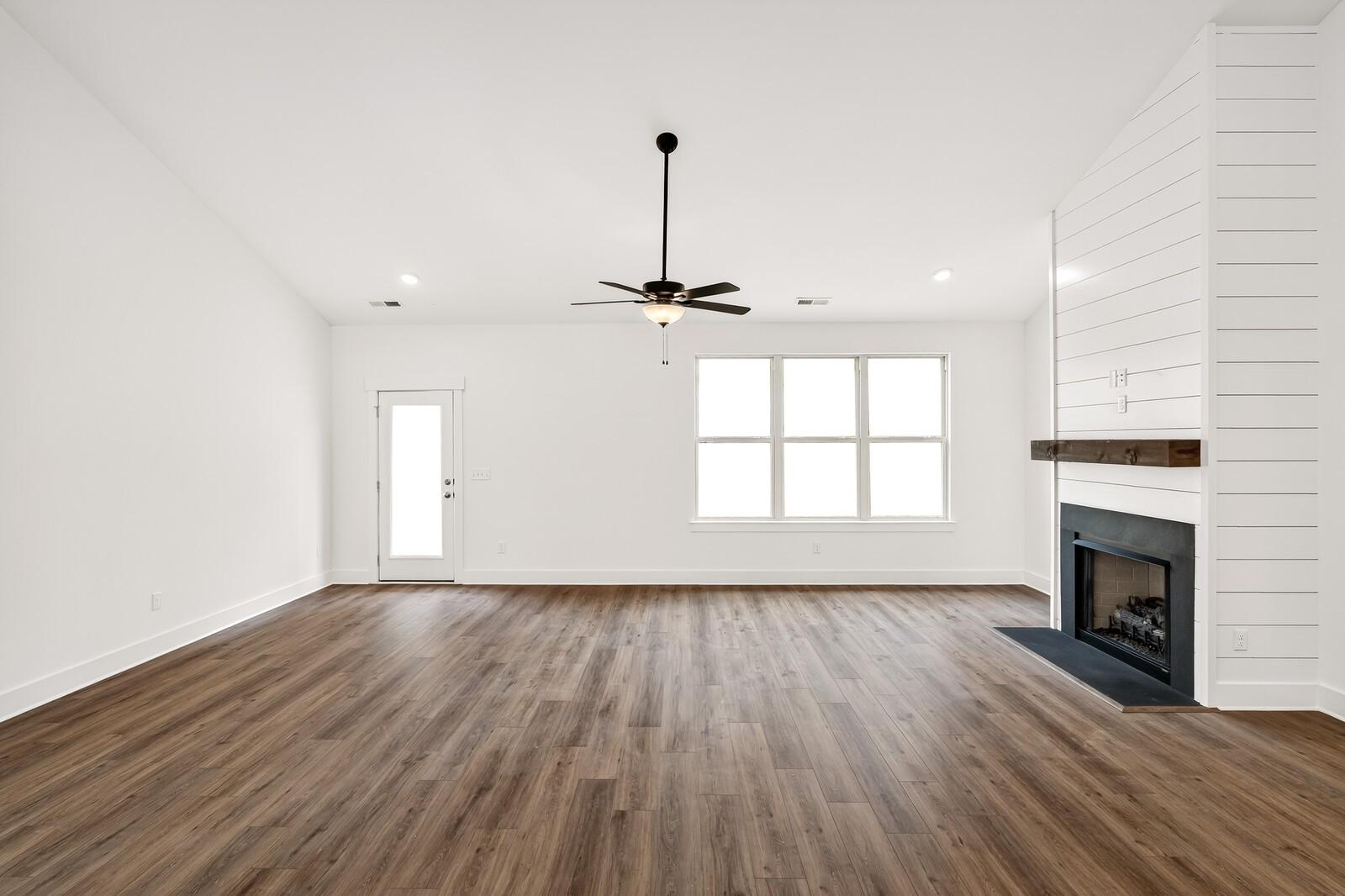 Bright living room with shiplap fireplace wall, large triple windows, ceiling fan, and hardwood floors in Davidson Homes Ridgeport C, Gallatin, TN
