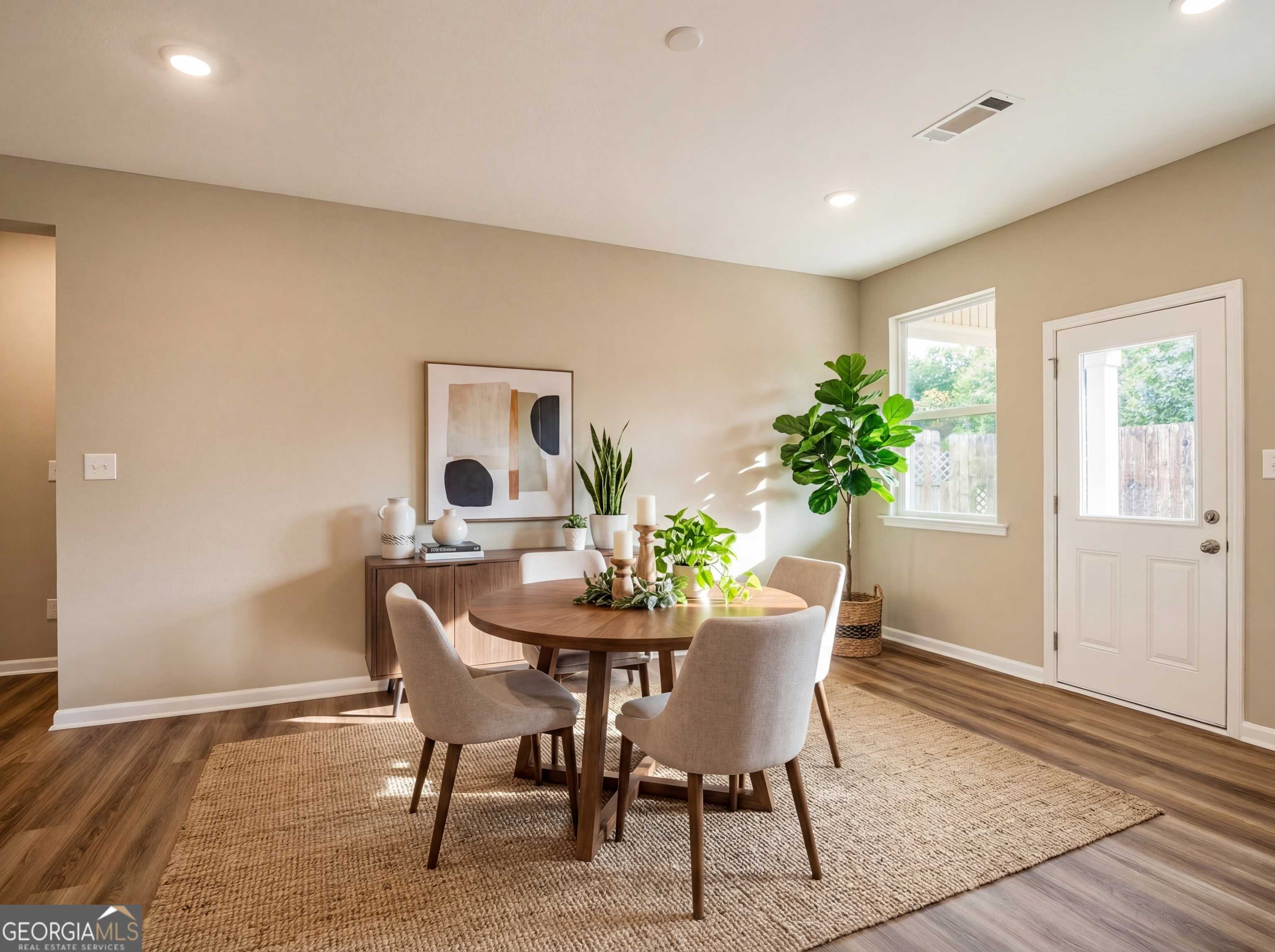 Modern dining room with round wooden table, beige chairs, potted plants, and abstract art in Evermore Homes The Luna, Perry, Georgia