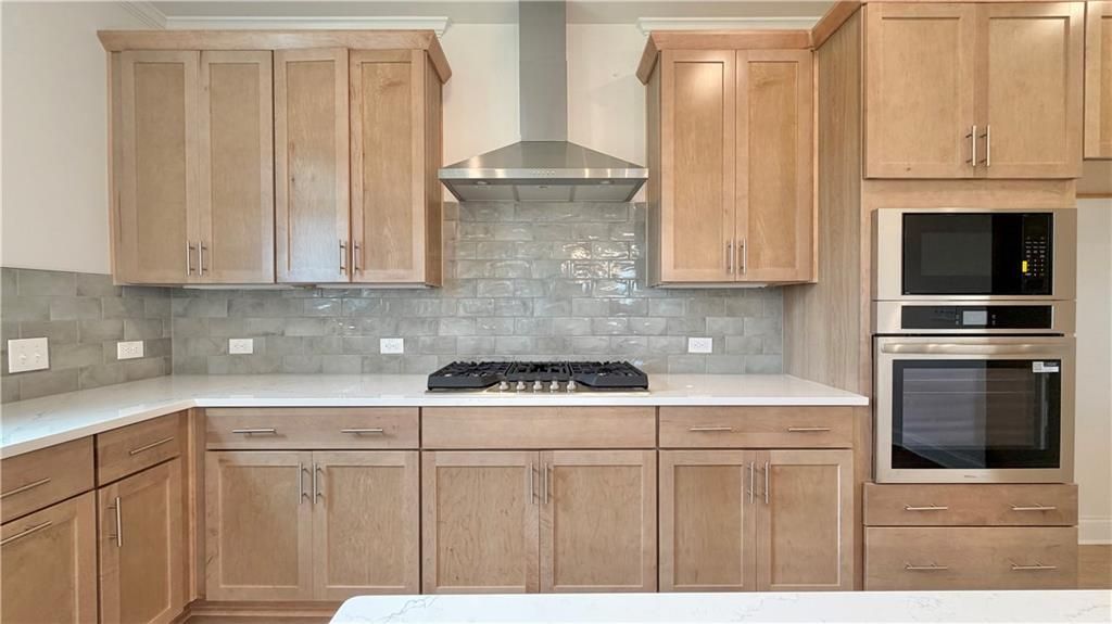Modern kitchen with natural wood cabinets, stainless steel appliances, and tile backsplash in The Hickory C, Hoschton, GA.