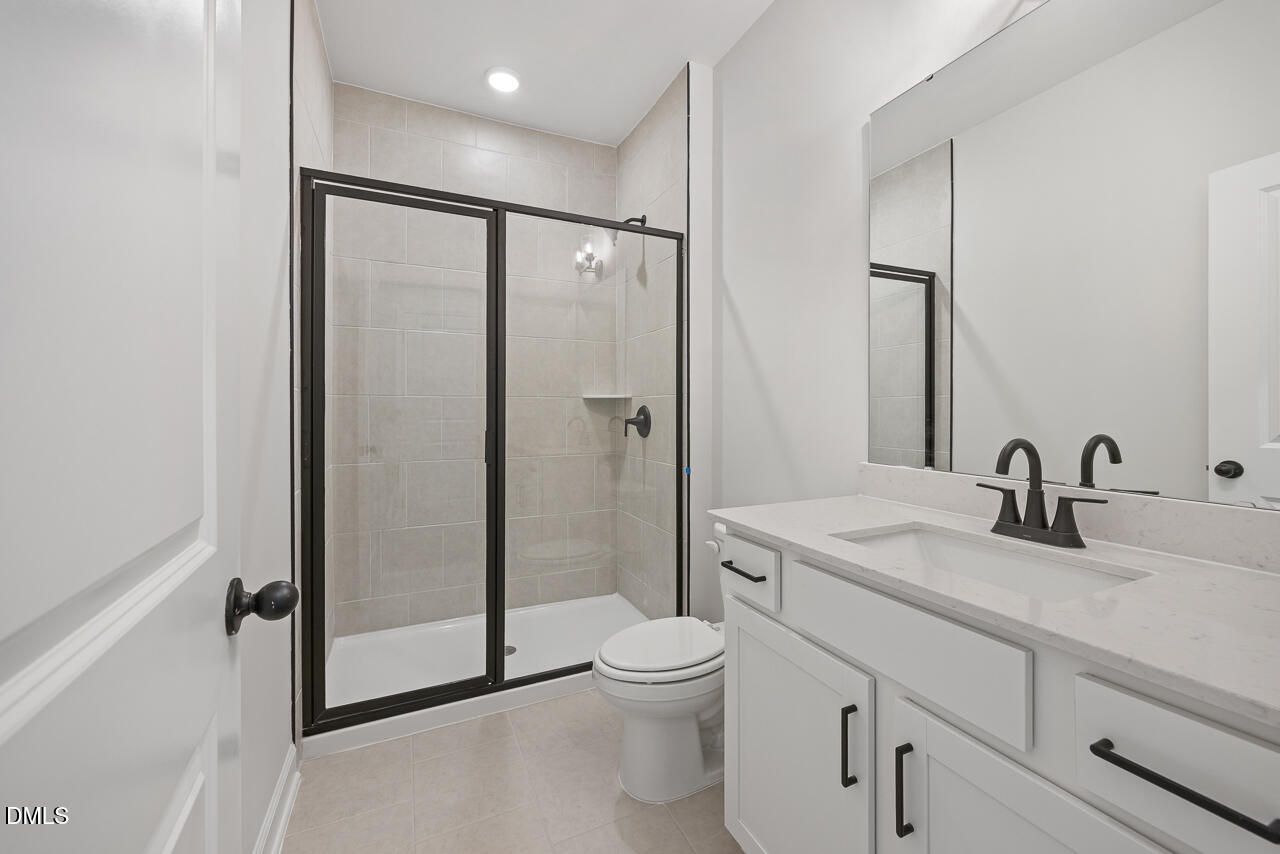 Modern white bathroom with glass walk-in shower, quartz vanity, and matte black fixtures in Davidson Homes The Preston C, Wendell Ridge NC