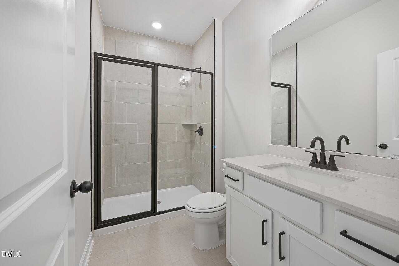 Modern white bathroom with glass walk-in shower, quartz vanity, and matte black fixtures in Davidson Homes The Preston C, Wendell Ridge NC