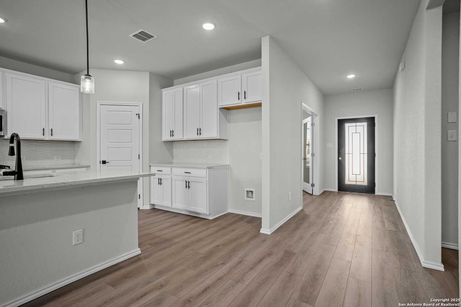 Modern white kitchen with large island, stainless faucet, and open hallway in Davidson Homes The Douglas B, Converse Texas