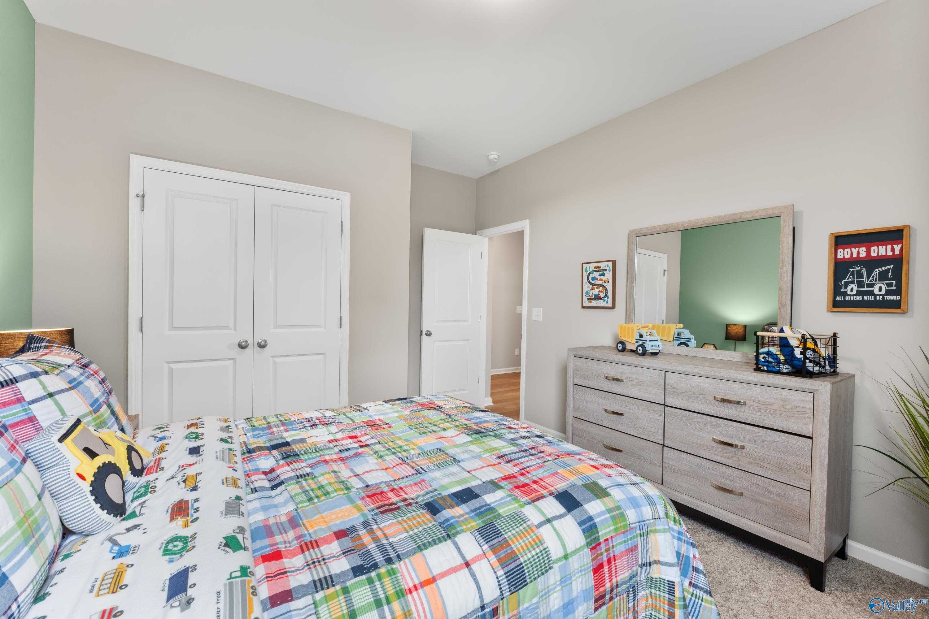 Cozy boys' bedroom with colorful truck bedding, wooden dresser, and mirrored vanity in Davidson Homes The Sanctuary, Athens, Alabama