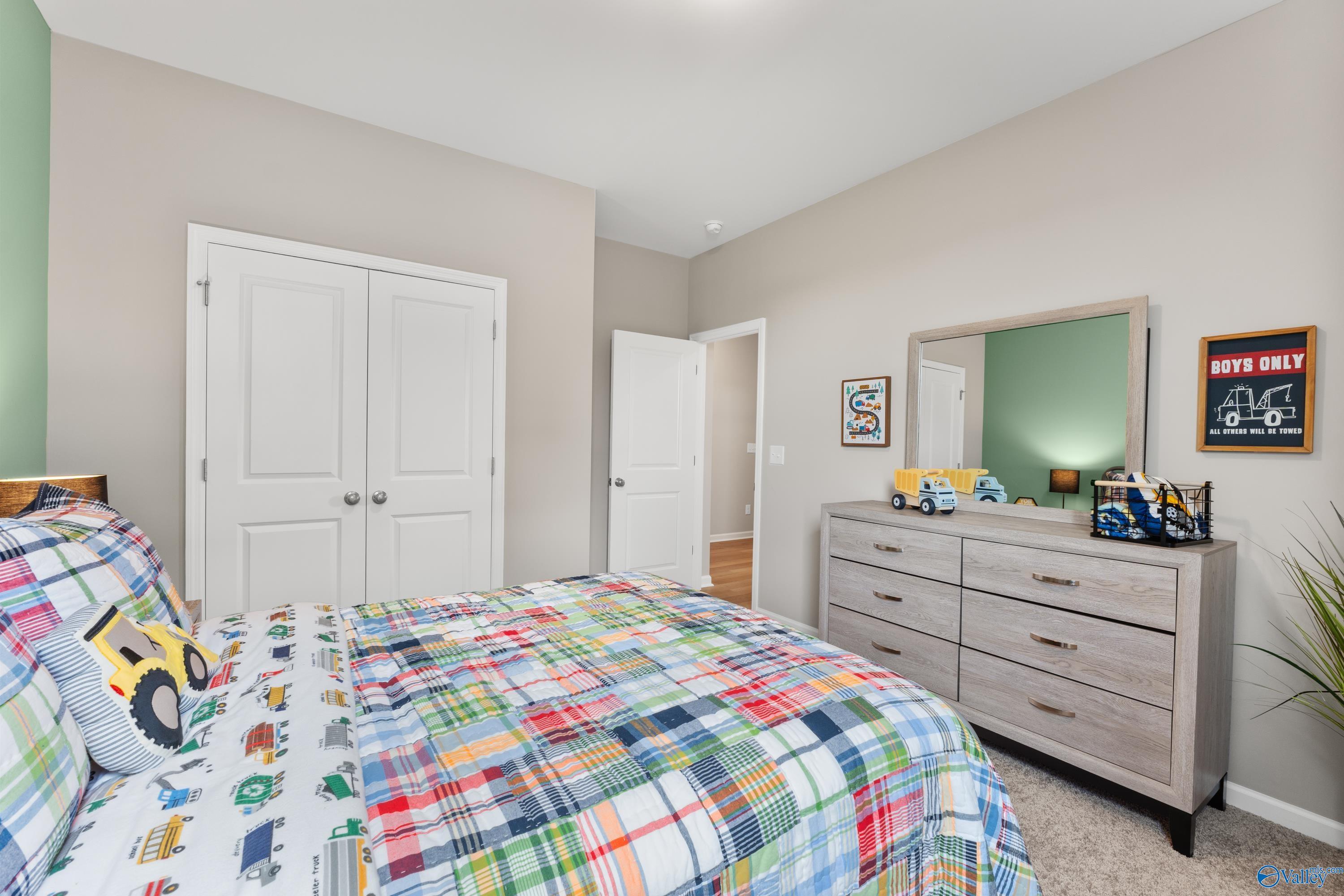 Cozy boys' bedroom with colorful truck bedding, wooden dresser, and mirrored vanity in Davidson Homes The Sanctuary, Athens, Alabama