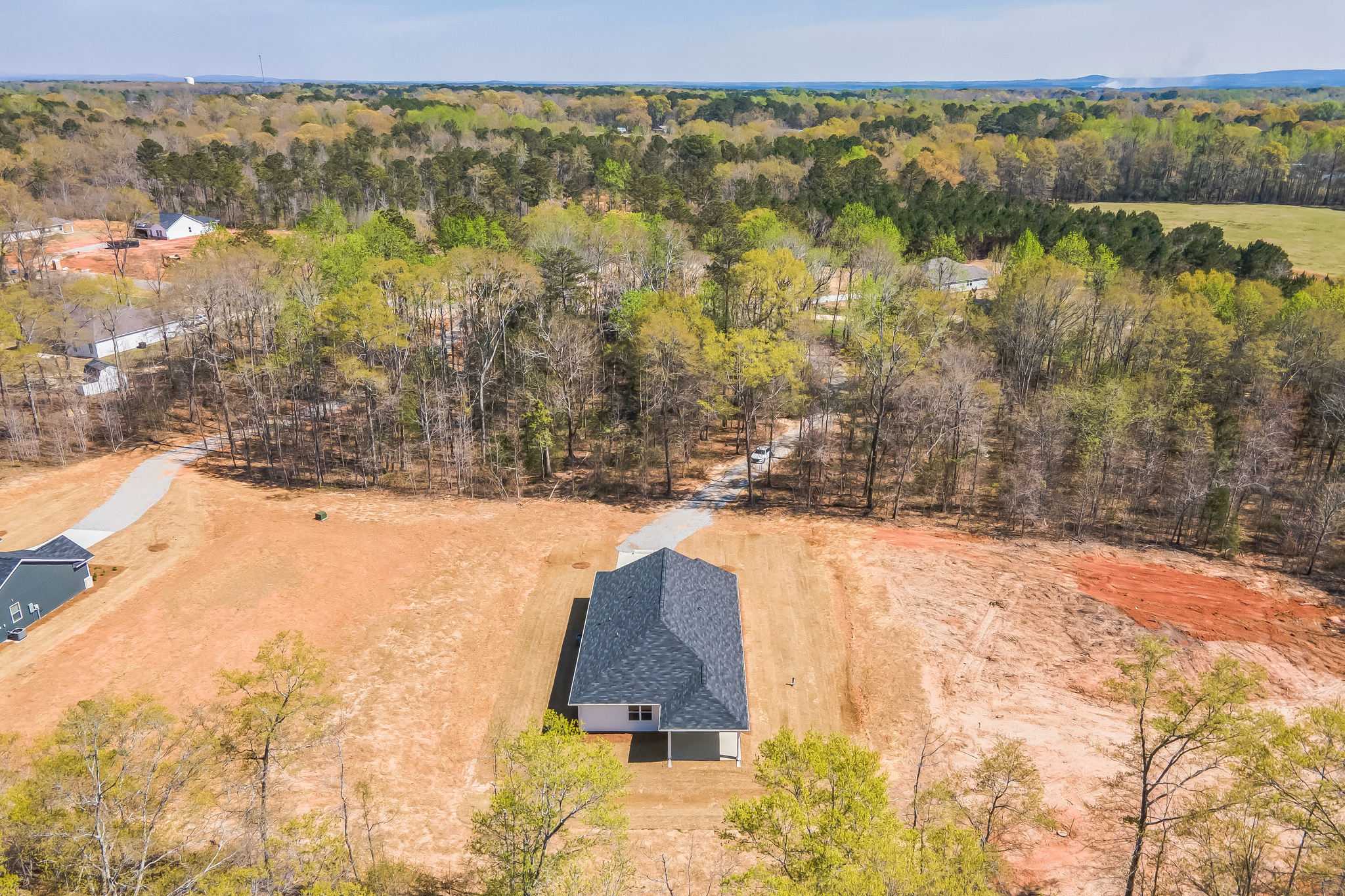 Aerial view of new single-story home with gray shingled roof at Silver Oak in Cusseta Alabama surrounded by wooded lots