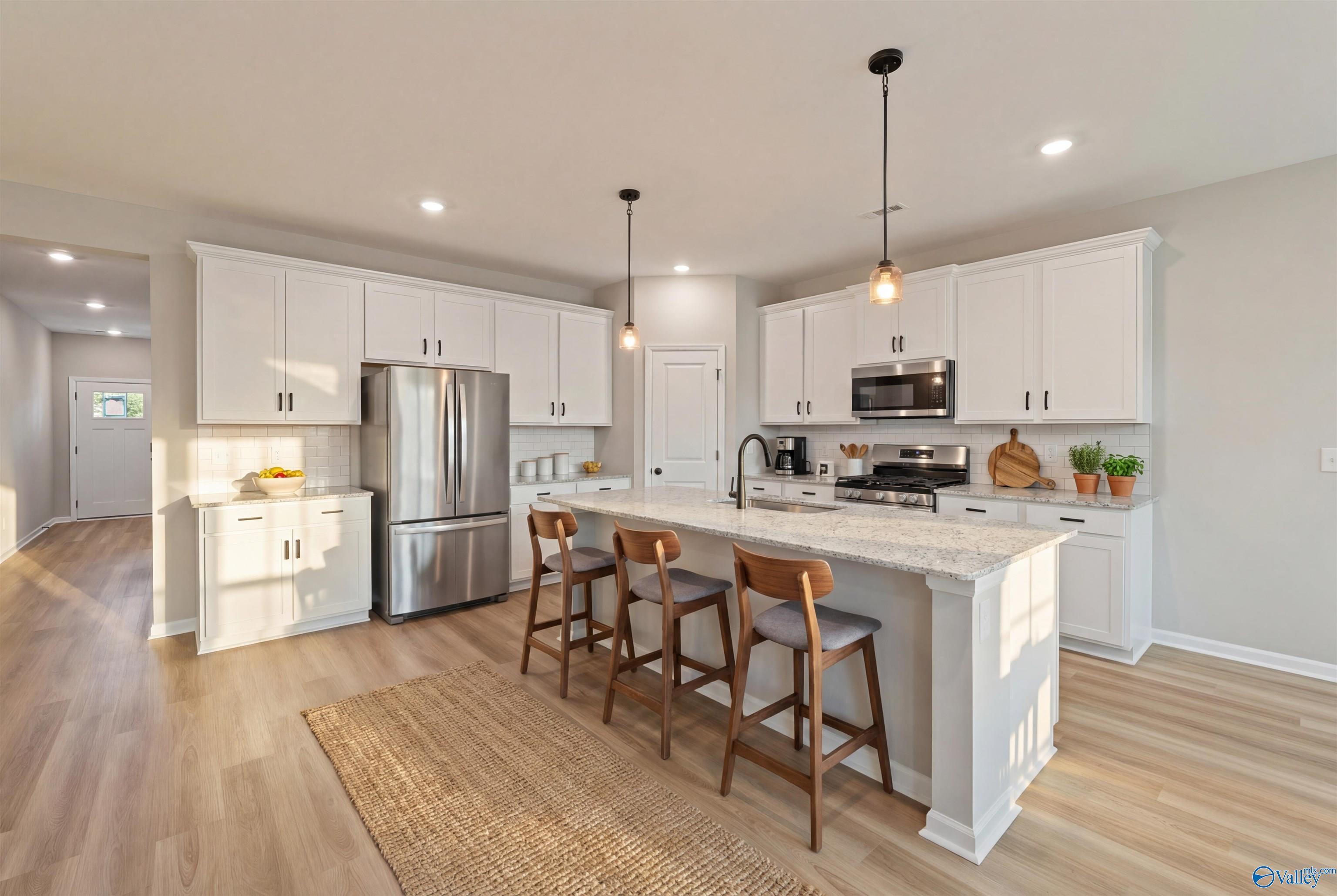 Modern white kitchen island with wooden bar stools, stainless appliances, and pendant lights in Davidson Homes The Phoenix, Hazel Green, AL