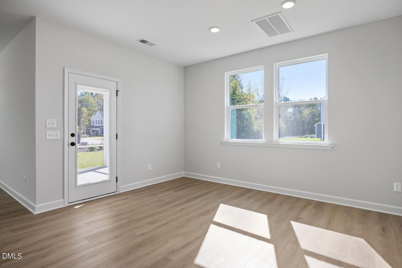 Bright empty room with luxury vinyl plank flooring, glass-panel door, and large windows in Davidson Homes The Preston C, Wendell Ridge, NC