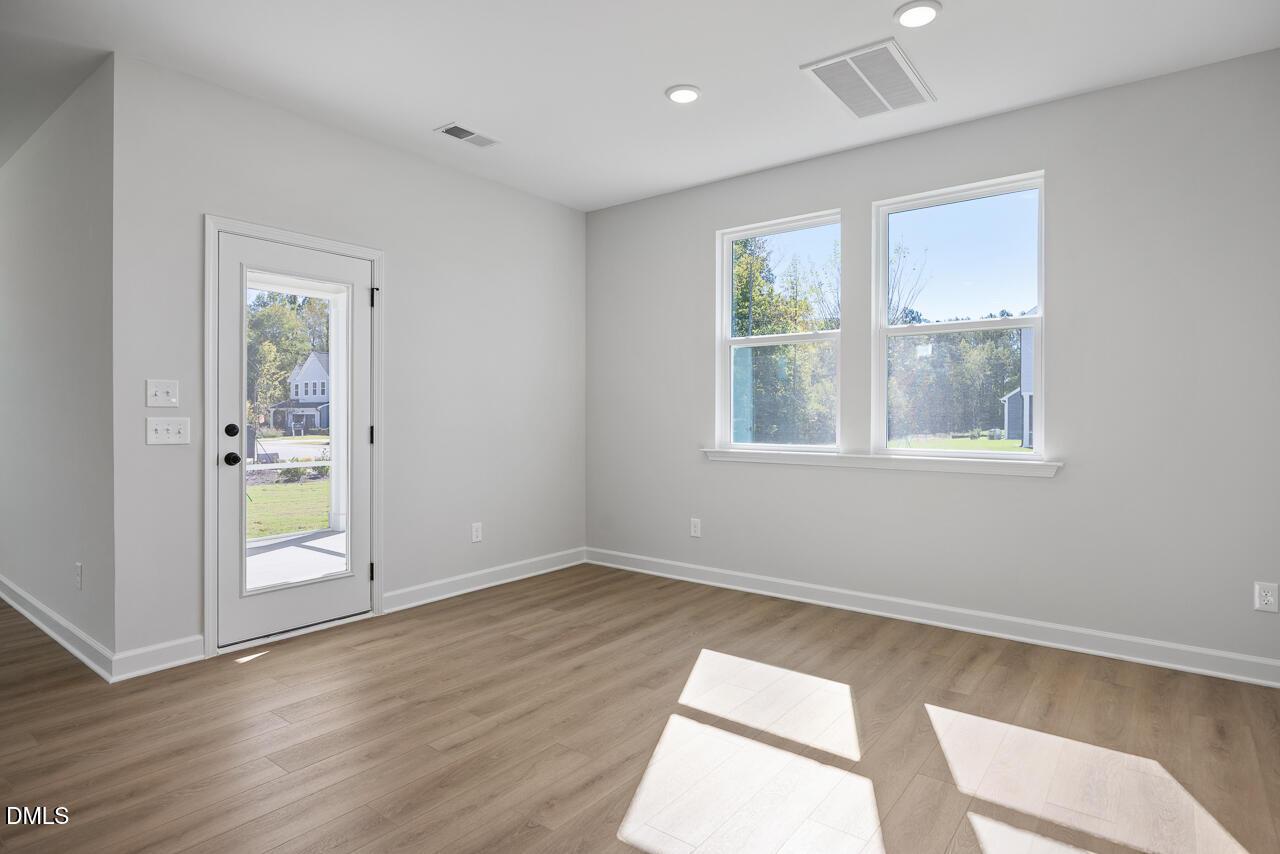 Bright empty room with luxury vinyl plank flooring, glass-panel door, and large windows in Davidson Homes The Preston C, Wendell Ridge, NC