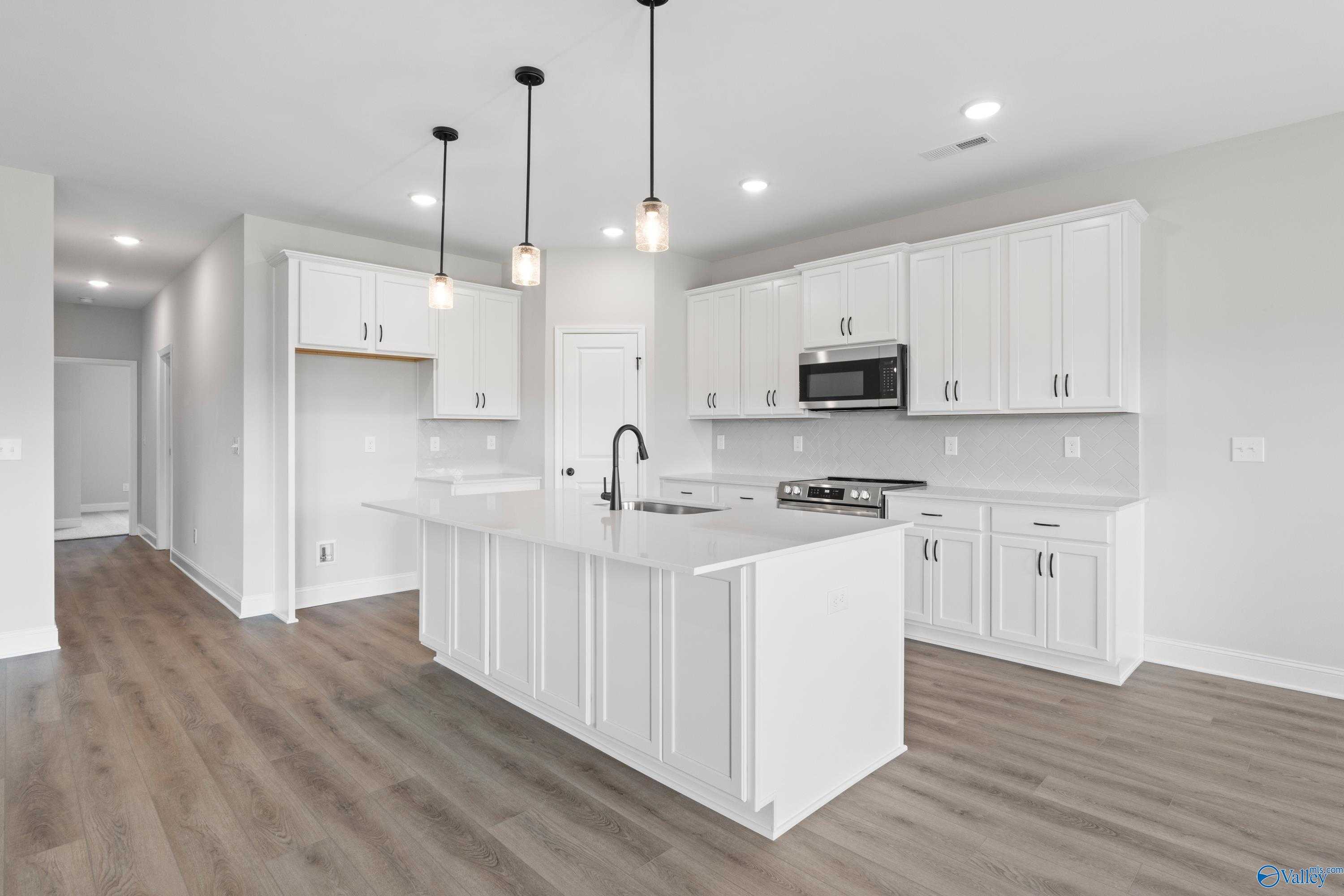 Bright open-concept kitchen with white shaker cabinets, large island sink, and stainless appliances in Davidson Homes The Rockford, Toney, AL