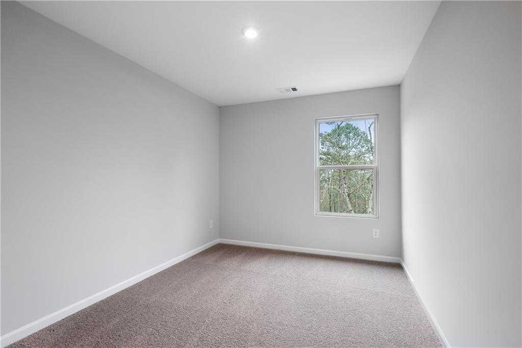 Bright empty bedroom with light gray walls, beige carpet, and large window overlooking trees in Davidson Homes The Durant A, Emerson, GA