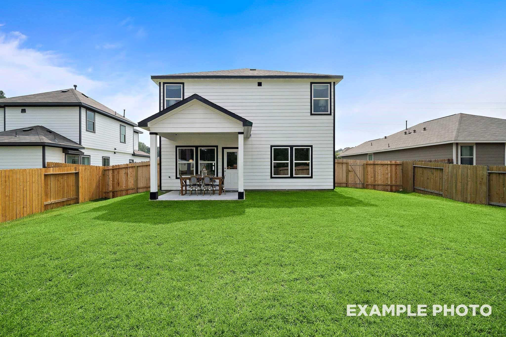 Rear view of two-story San Marcos E home featuring covered patio, seating, and lush fenced backyard in Conroe, Texas
