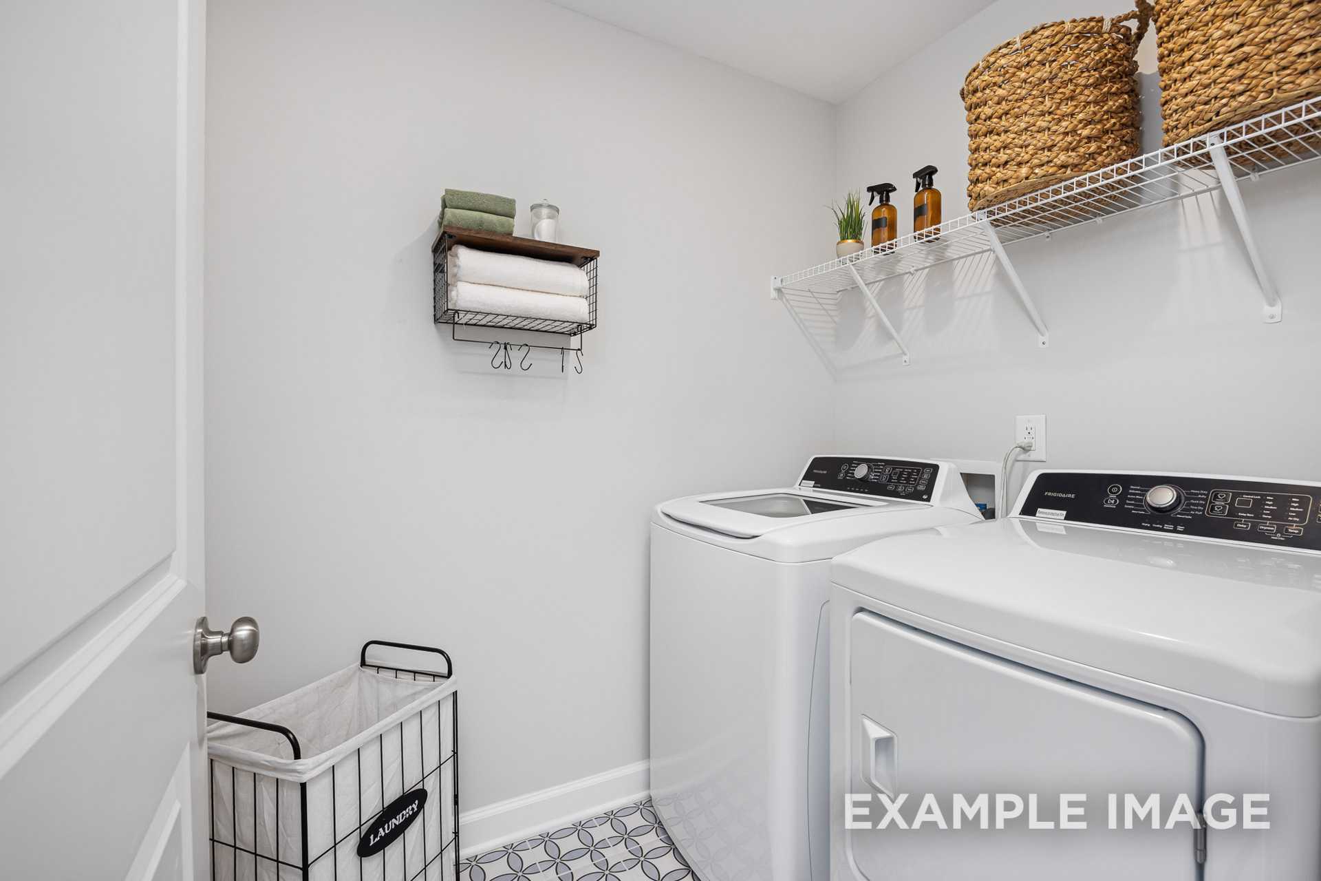 Bright laundry room in The Adalynn A with white washer-dryer set, wire shelves, towels, and woven baskets by Davidson Homes