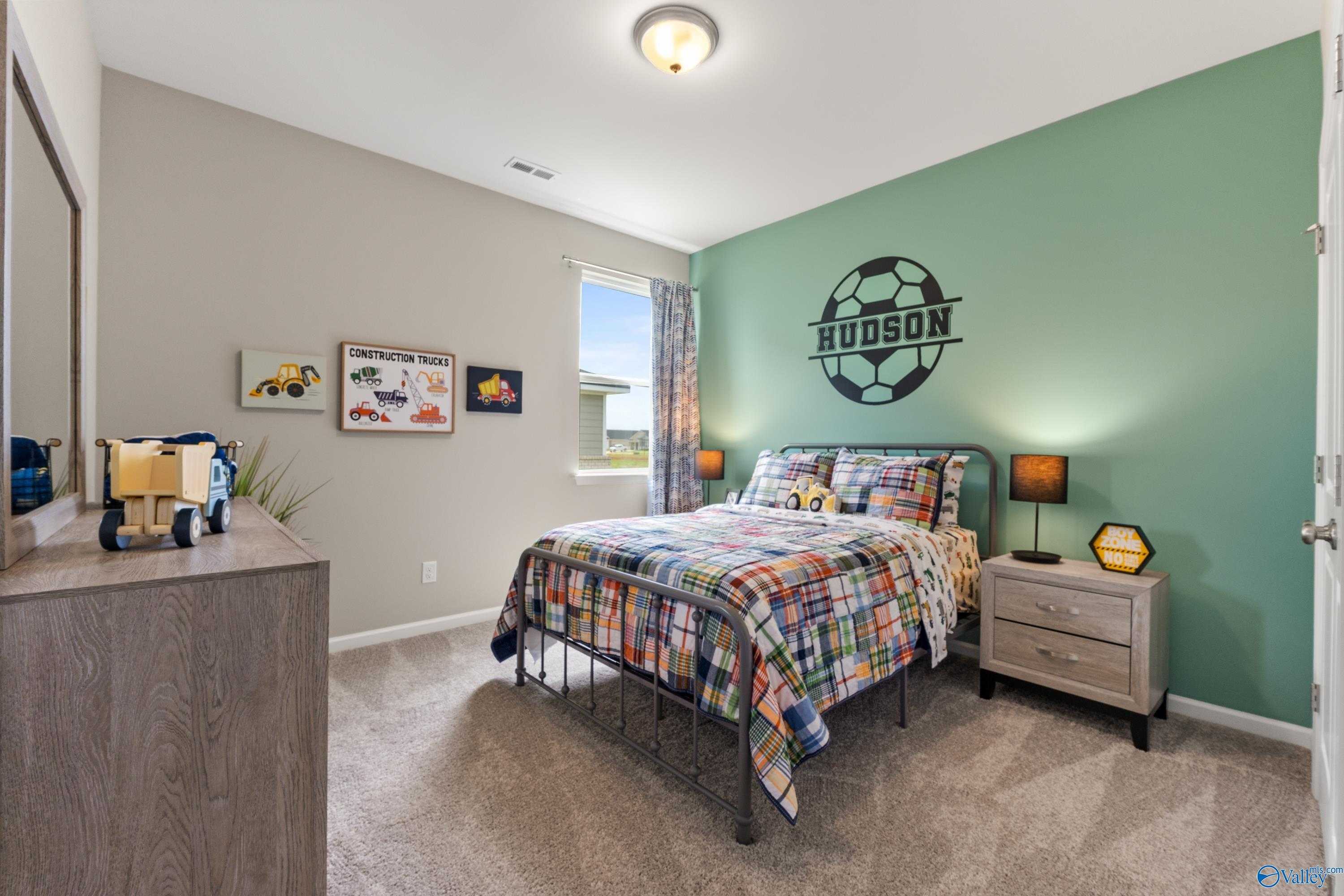 Cozy boy's bedroom with soccer decal, colorful plaid bedding, toys, and green accent wall in Davidson Homes The Sanctuary, Athens, AL