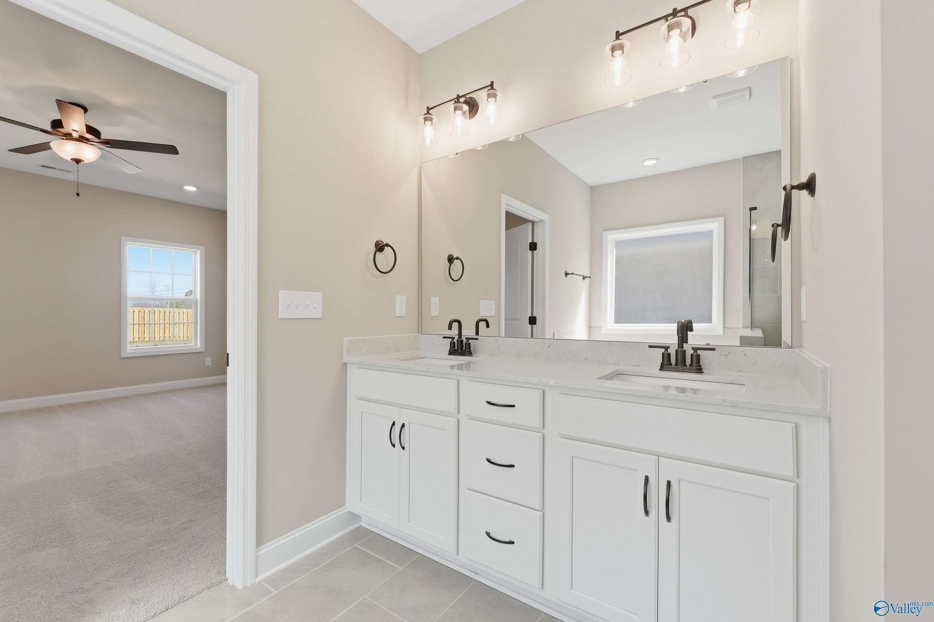 Elegant master bathroom with double white vanity, quartz countertop, and lighted mirror in Davidson Homes The Rockford, Harvest AL