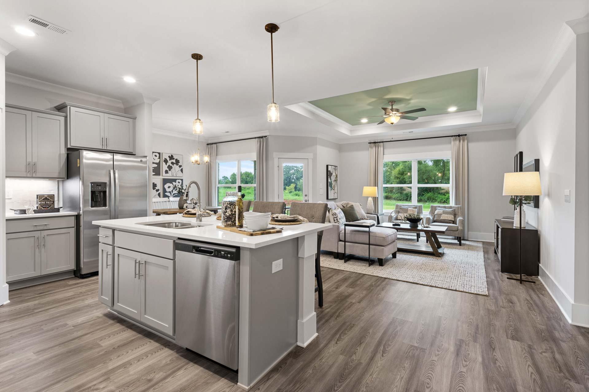 Open-concept kitchen living room in The Meadows Athens AL with white shaker cabinets stainless steel island hardwood floors and large windows