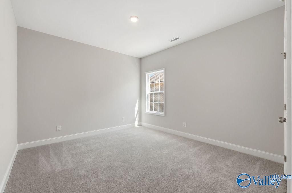 Spacious empty bedroom with light gray walls, plush carpet, large sunny window in Davidson Homes The Harrison, Hartselle AL