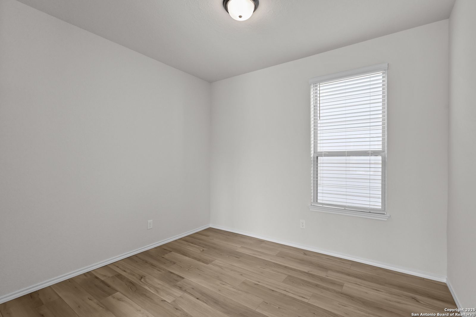 Bright secondary bedroom with white walls, blinds window, ceiling light, and hardwood floors in Davidson Homes Florence C, San Antonio