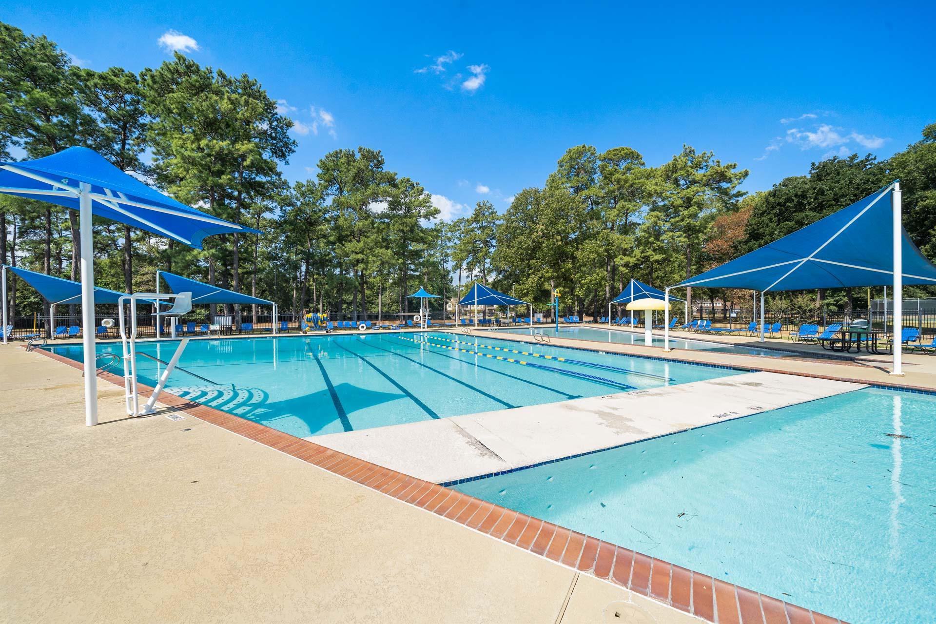 Community swimming pool at Enclave at Newport in Crosby, Texas with blue umbrellas, lounge chairs, and lane dividers
