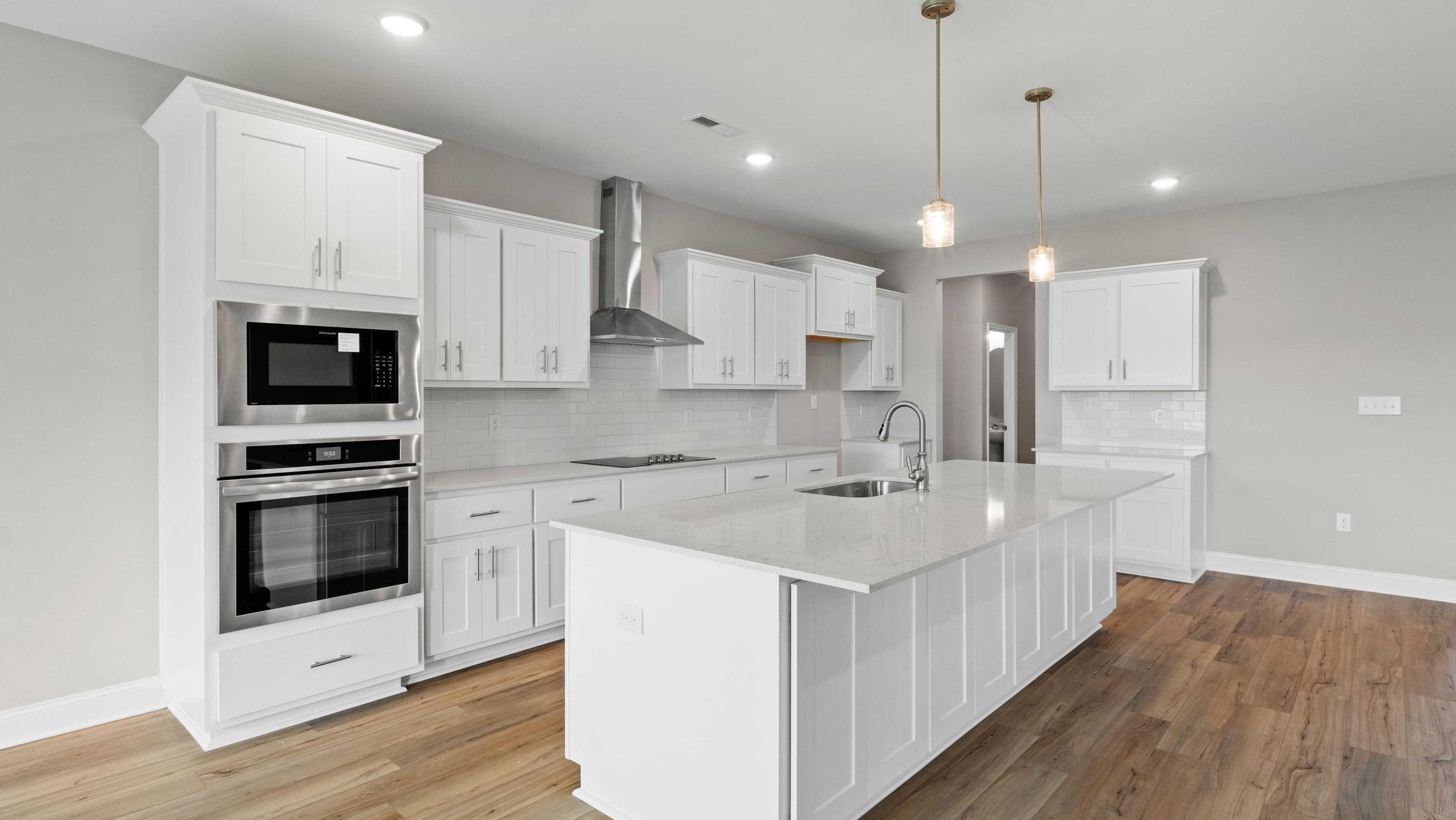 Modern white kitchen with quartz island, stainless appliances, recessed lighting, hardwood floors in Davidson Homes model home