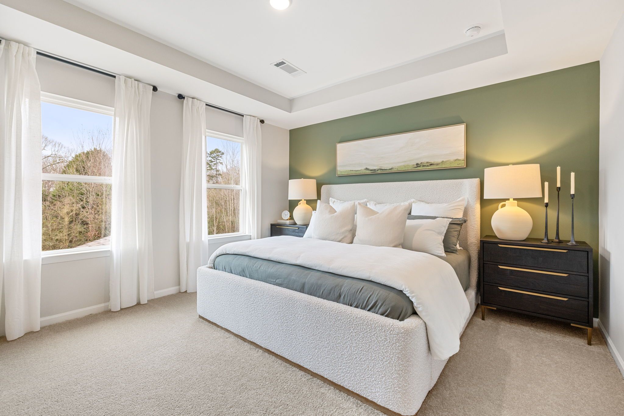 Elegant primary bedroom at Links Crossing in Auburn AL with white tufted bed, sage green accent wall, and large curtained windows