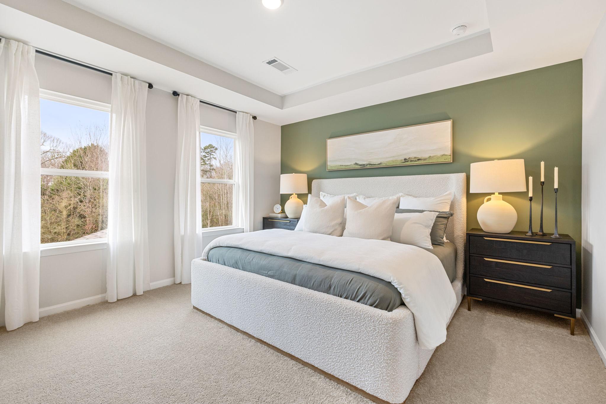 Elegant primary bedroom at Links Crossing in Auburn AL with white tufted bed, sage green accent wall, and large curtained windows