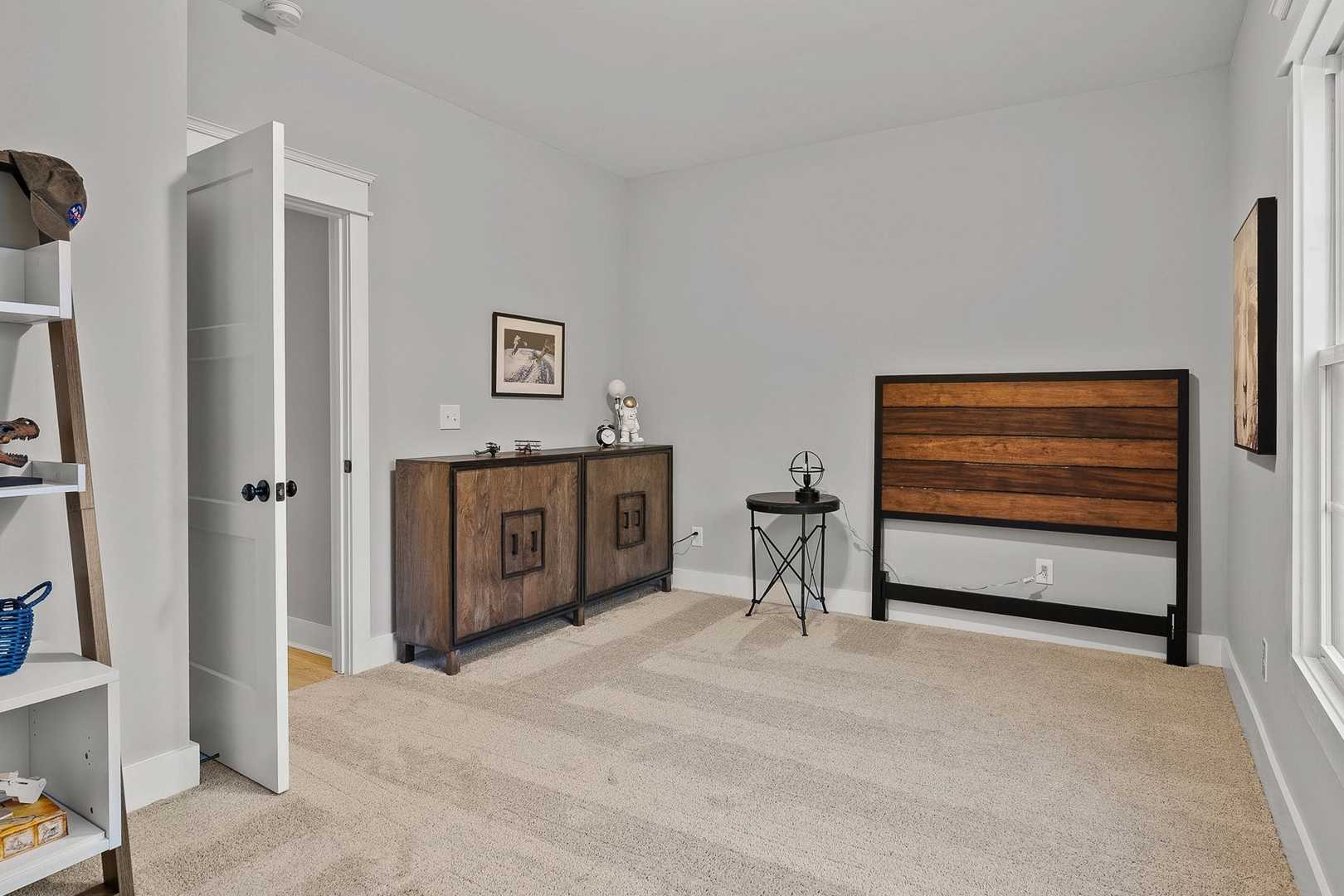 Spacious bedroom in The Oxford home design featuring wooden headboard bed, white bookshelves, and gray walls with large windows