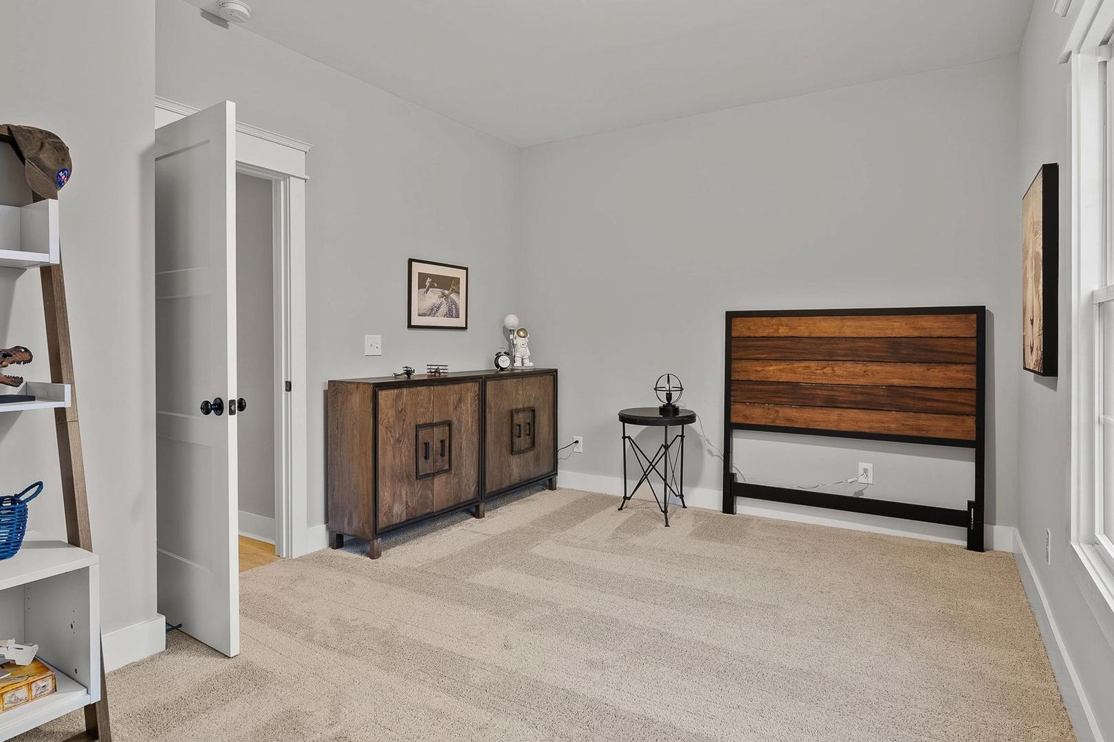Spacious bedroom in The Oxford home design featuring wooden headboard bed, white bookshelves, and gray walls with large windows